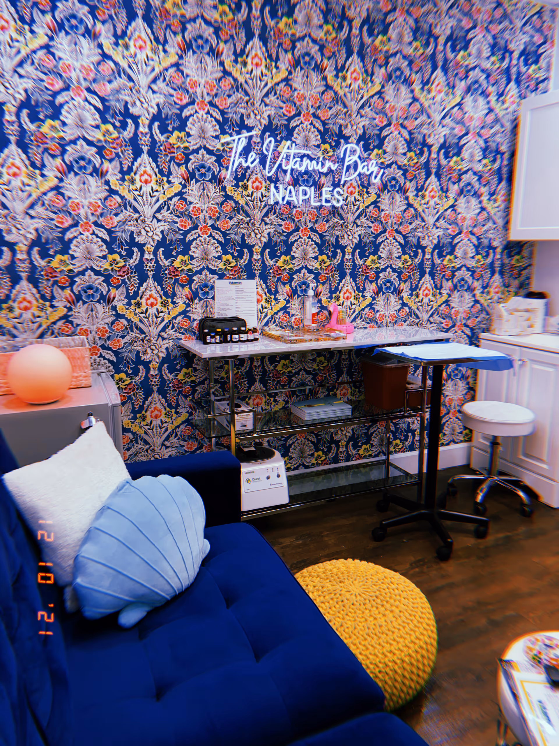 The Vitamin Bar Naples sign on ornate blue wallpaper beside a blue couch.