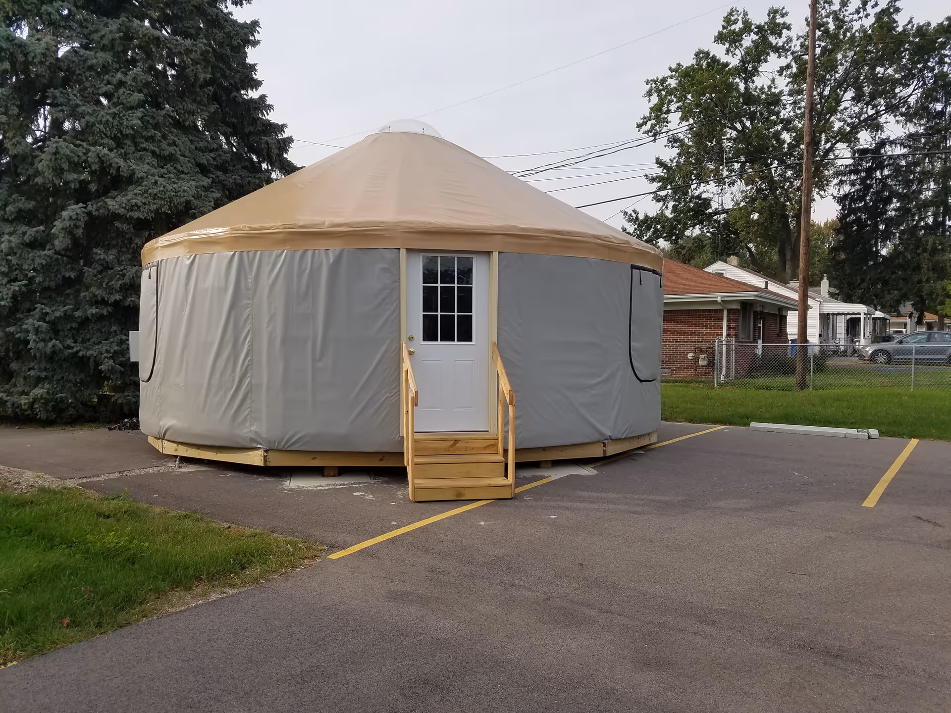 Round beige-topped tent with gray walls, white door, and wooden steps in a parking lot.