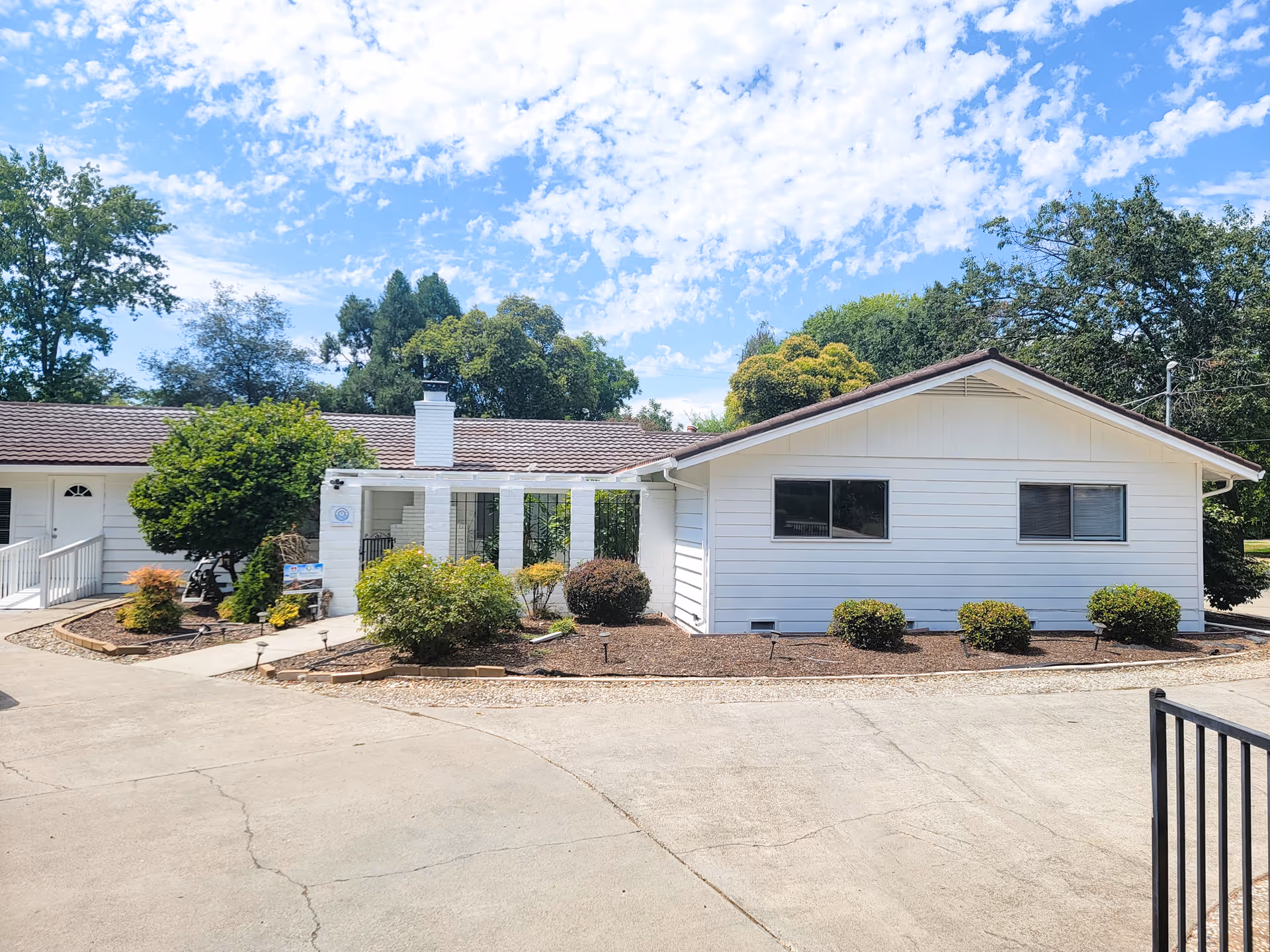 White single-story senior living facility with manicured shrubs and a paved driveway.