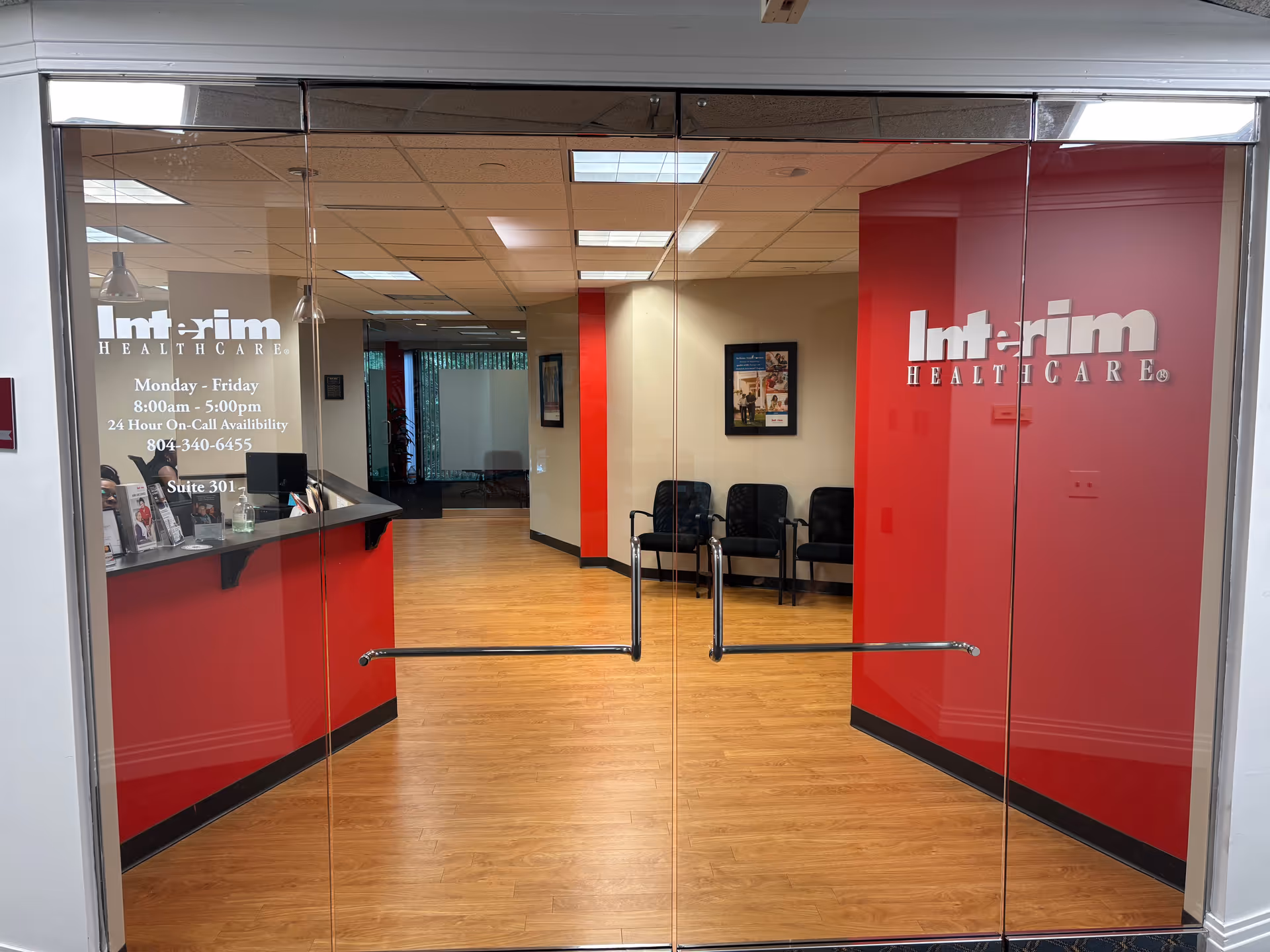 Glass doors reveal Interim HealthCare lobby with red walls, reception desk, and seating.