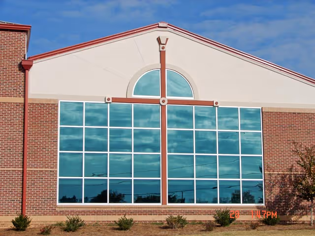 Exterior view of a brick senior living facility with large glass windows and decorative cross design.