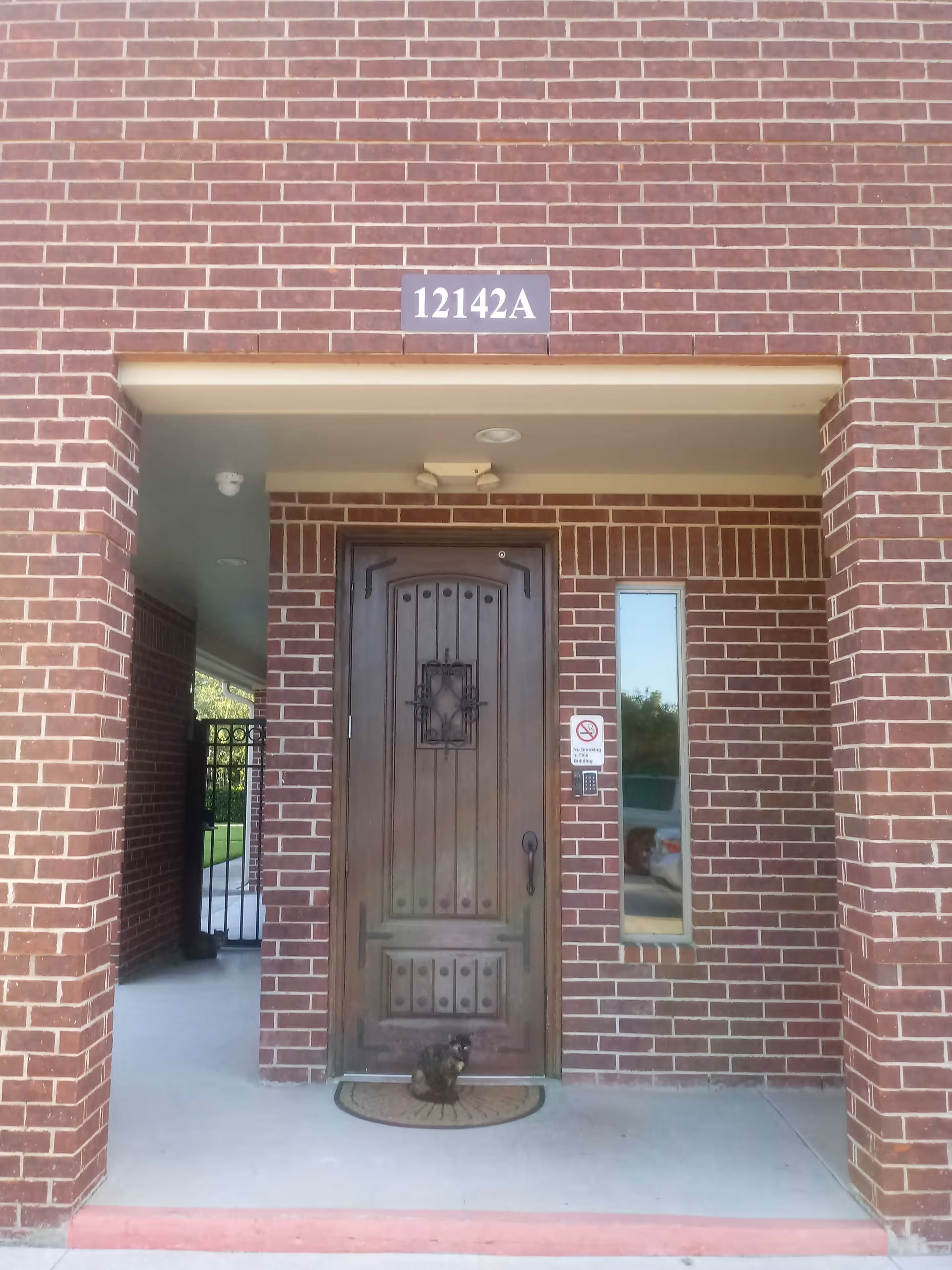 Brick building entrance with a wooden door, window, and address plaque 12142A.