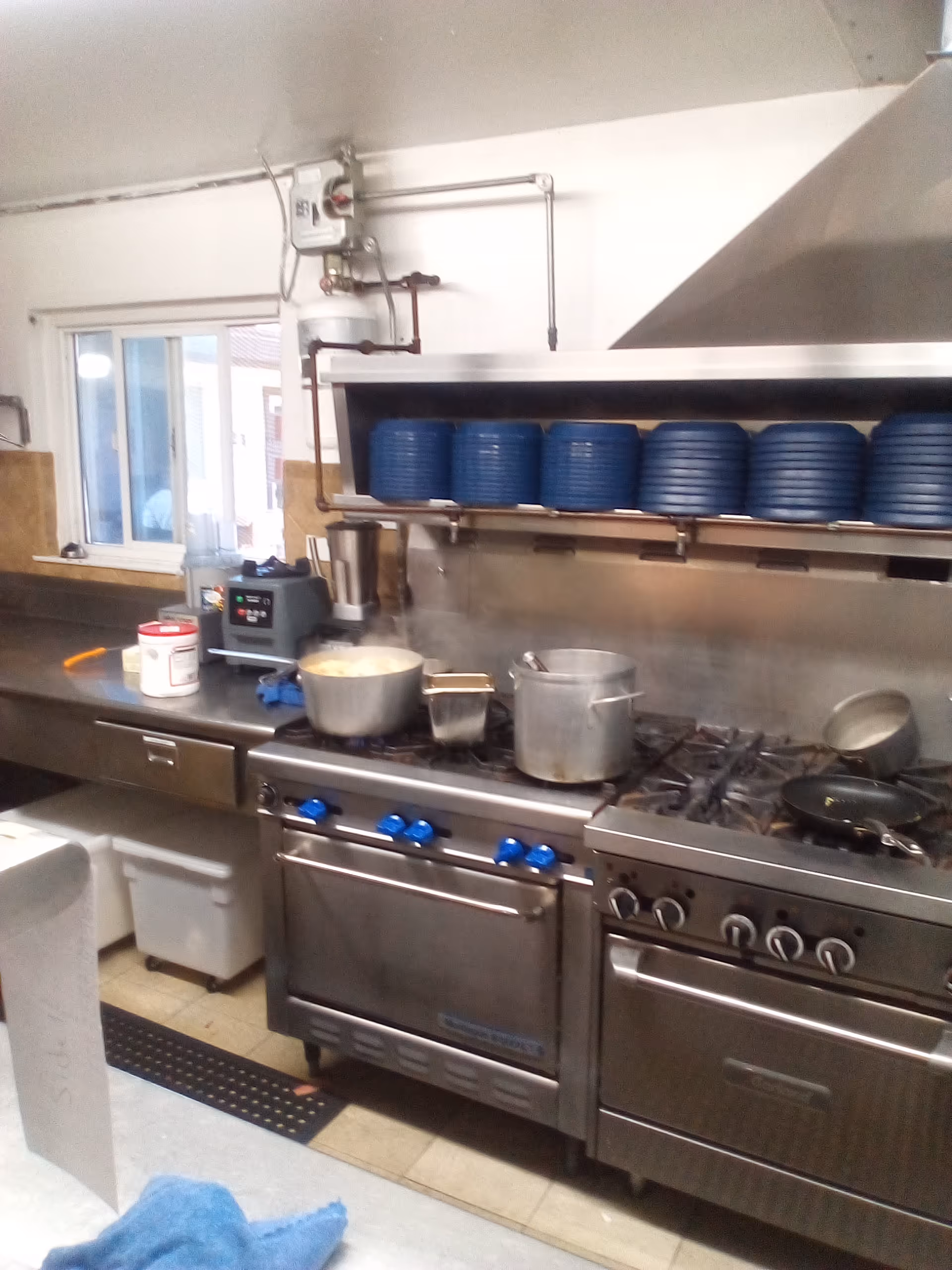 Commercial kitchen with stainless steel appliances, stacked blue bowls, and pots on the stove.