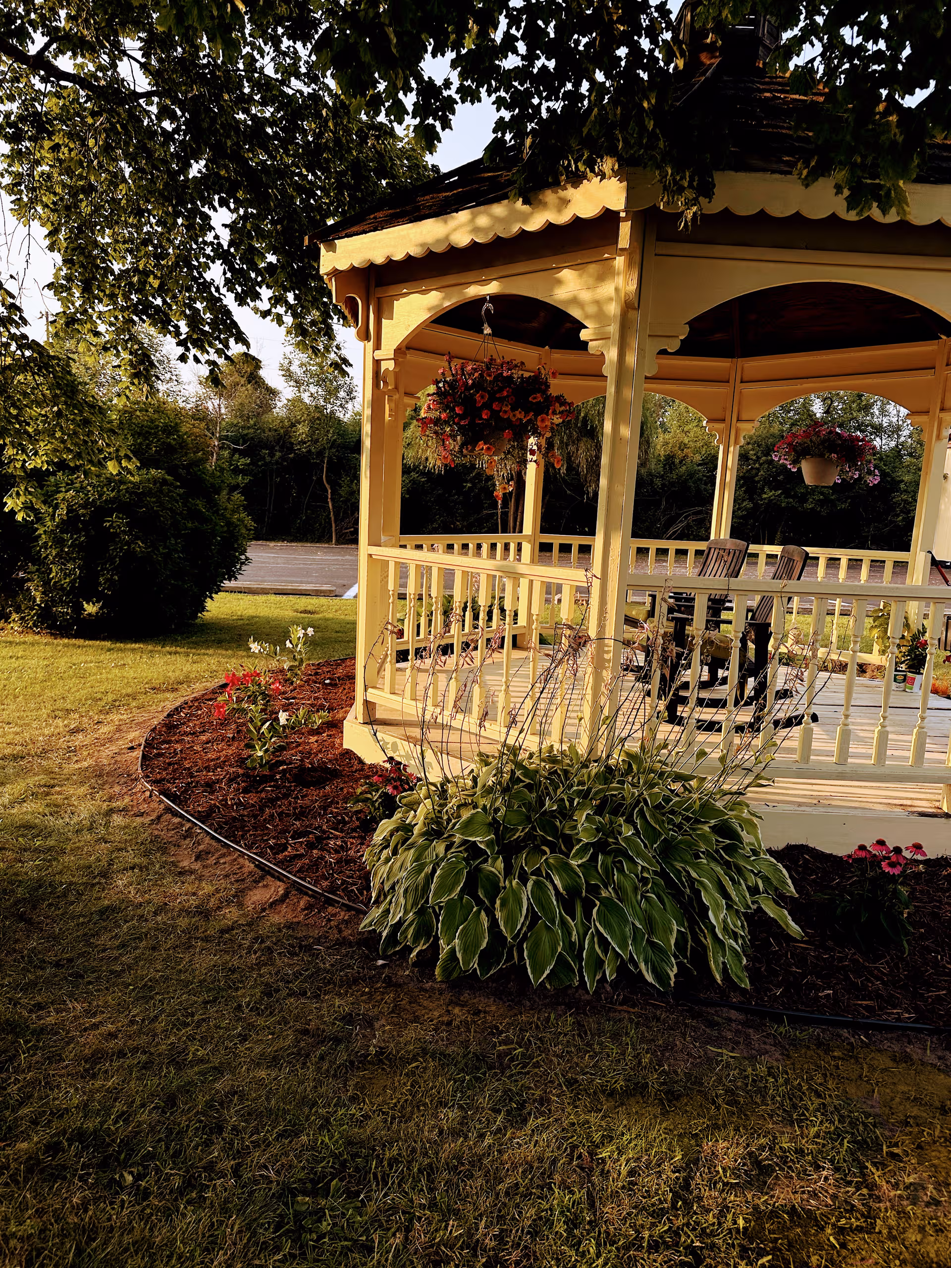 Exterior view of a yellow gazebo with hanging baskets on a manicured lawn.