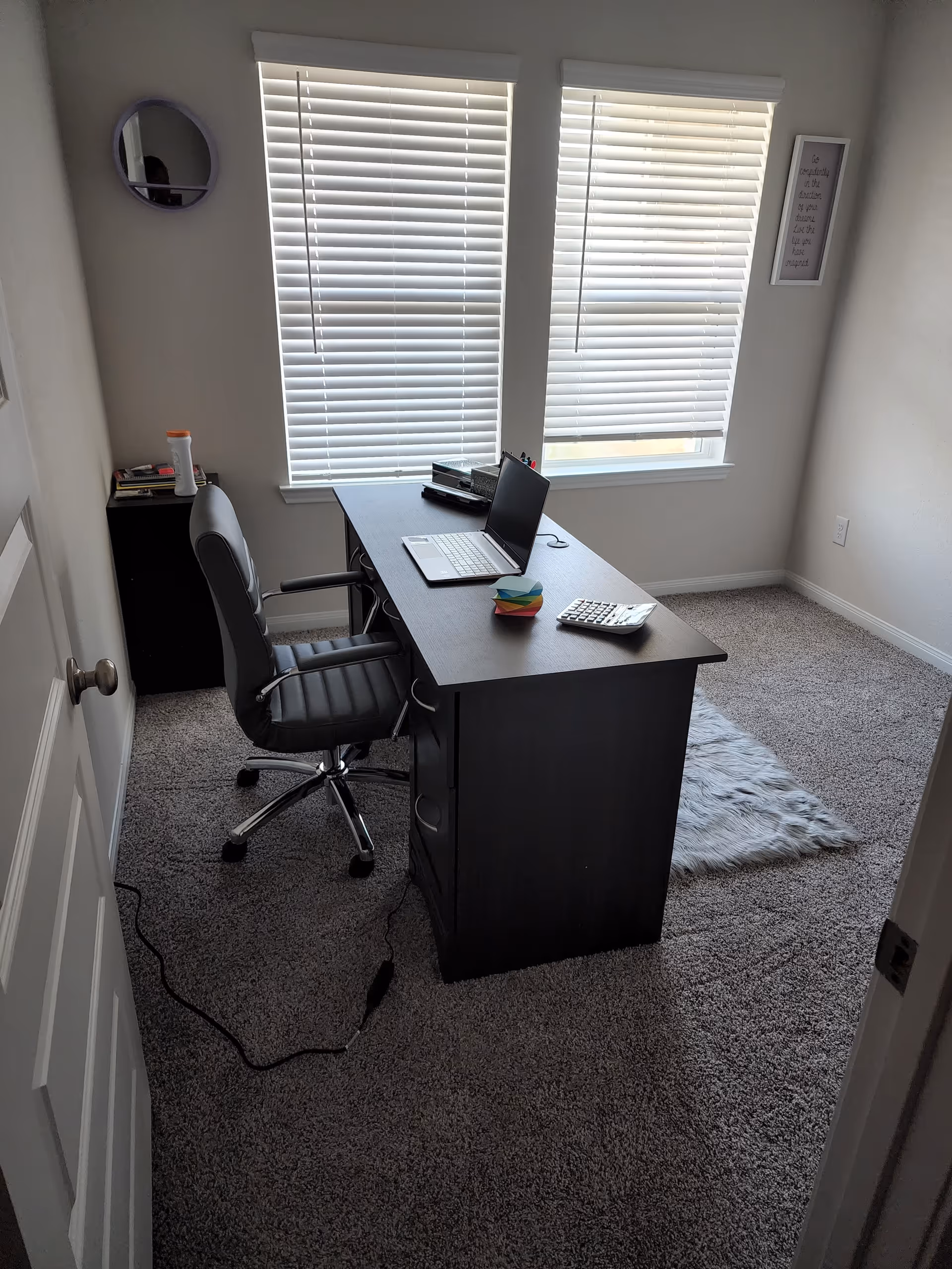 Interior home office in a senior living facility with desk, laptop, and blinds.