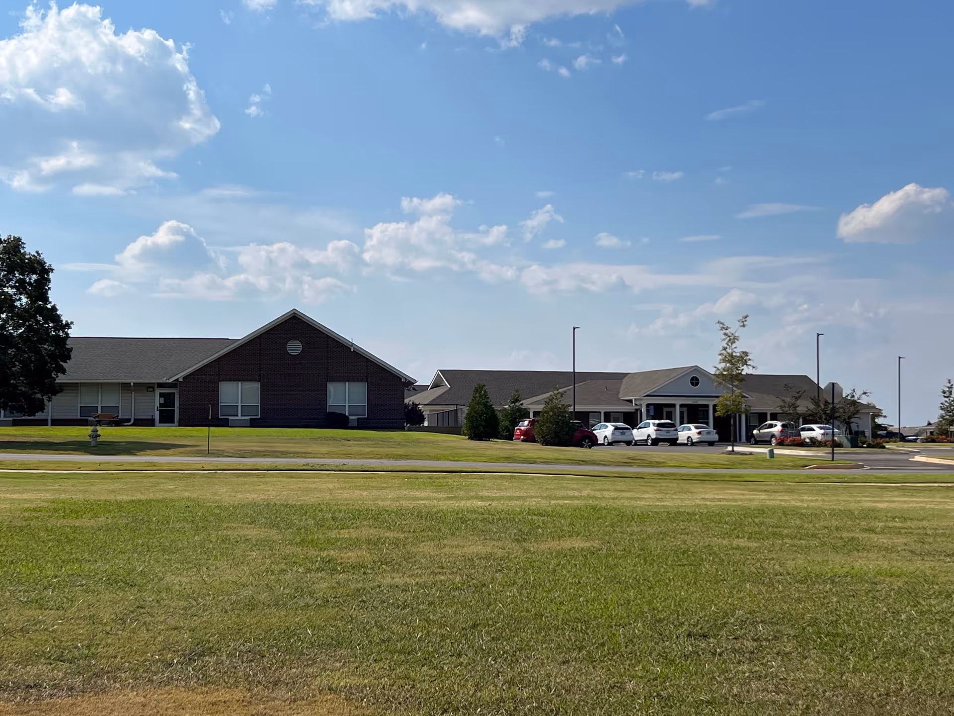 Wide view of a senior living facility exterior with a parking lot and blue sky.