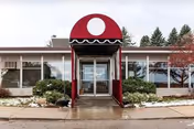 Front entrance of a senior living building with a red arched canopy and glass doors.