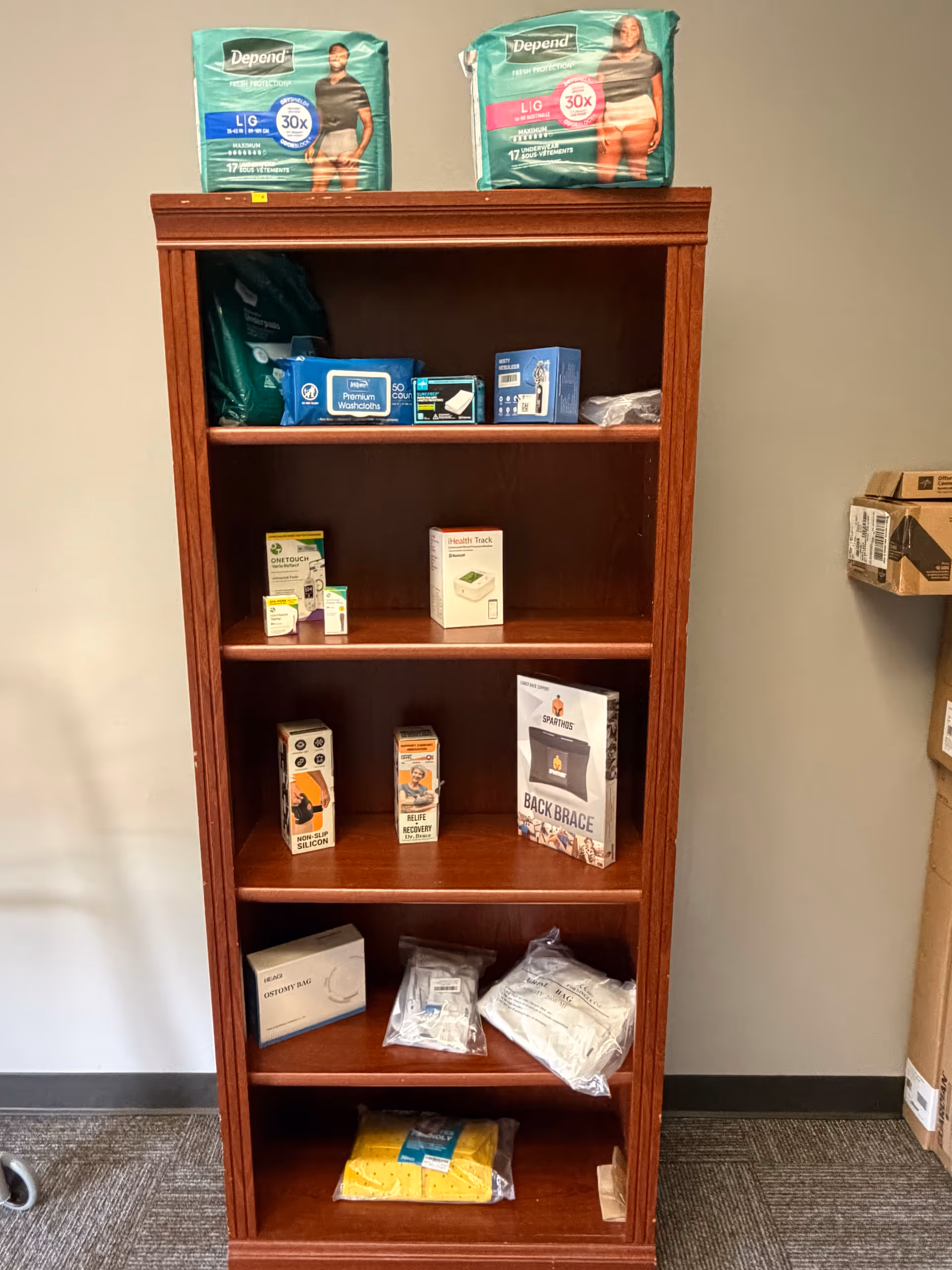 Wooden bookshelf stocked with medical supplies and disposable diapers in a facility corridor.
