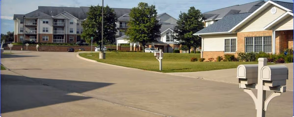 Senior living campus exterior with brick buildings, mailboxes, and a curved driveway.