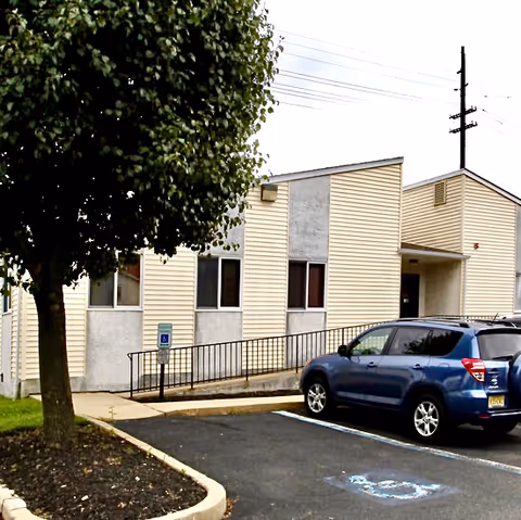 Exterior view of a senior living facility with a parking lot and blue SUV.