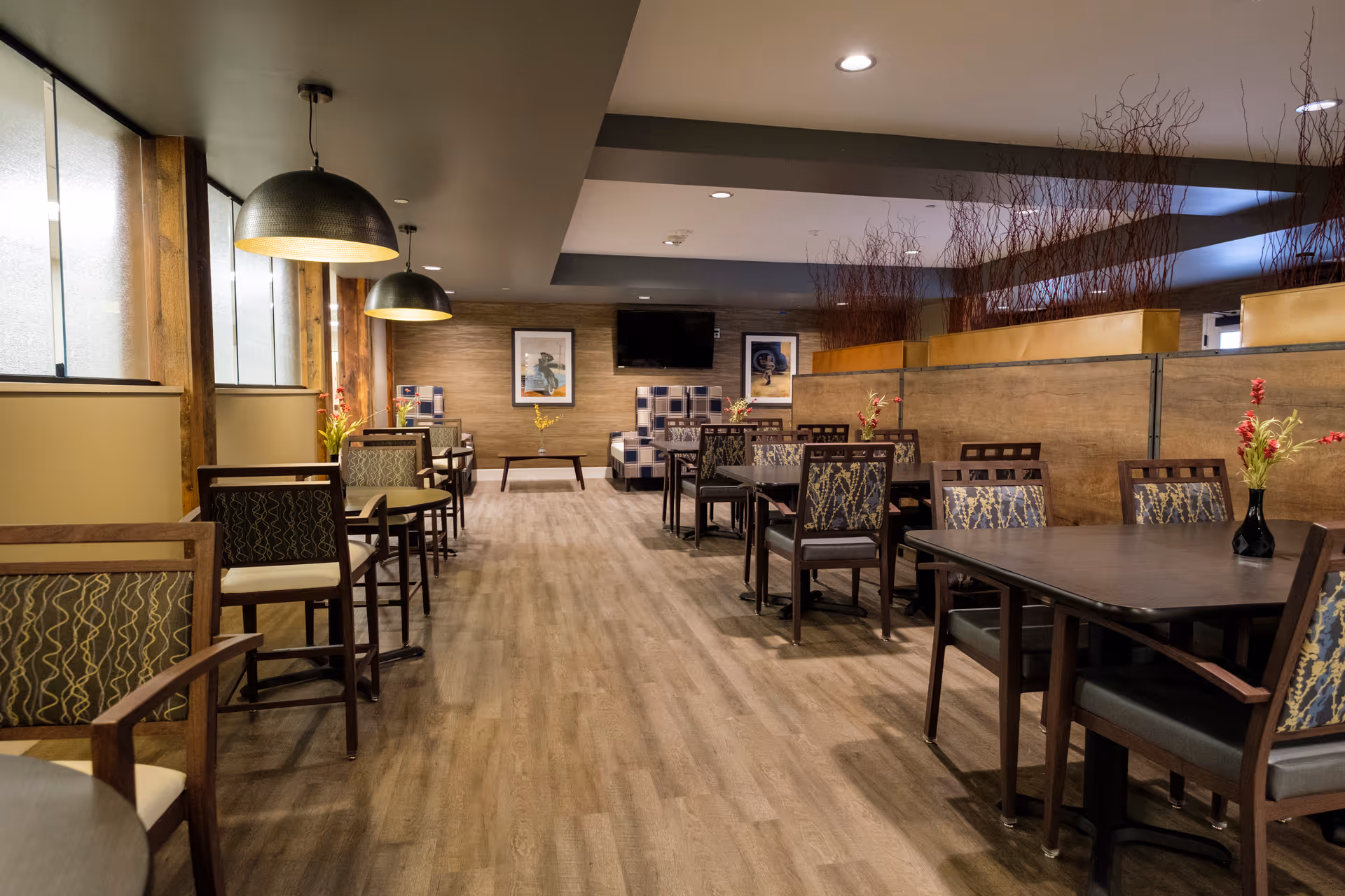 Spacious dining room in a senior facility with dark wood tables and patterned chairs.