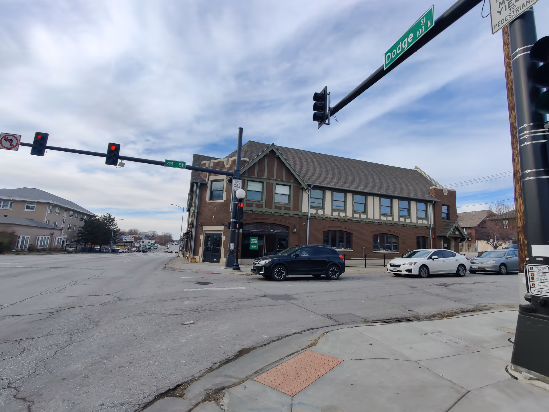 Corner brick building with traffic signals, parked cars, and a crosswalk.