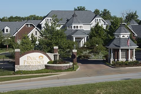 Front view of Parc Provence senior living facility with sign, entrance, and landscaped grounds.