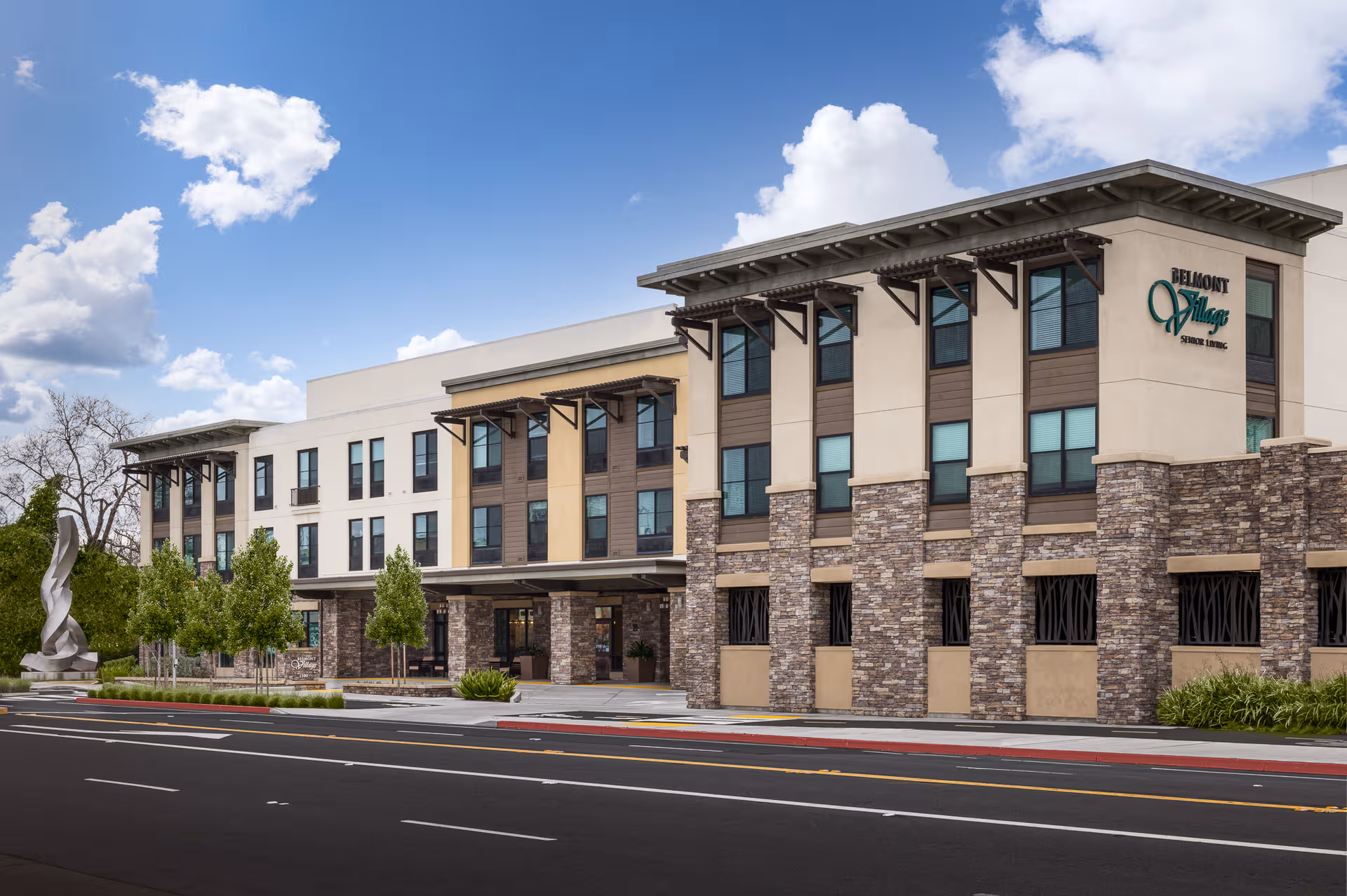 Front exterior of Belmont Village Senior Living Albany, with stone columns and blue sky.