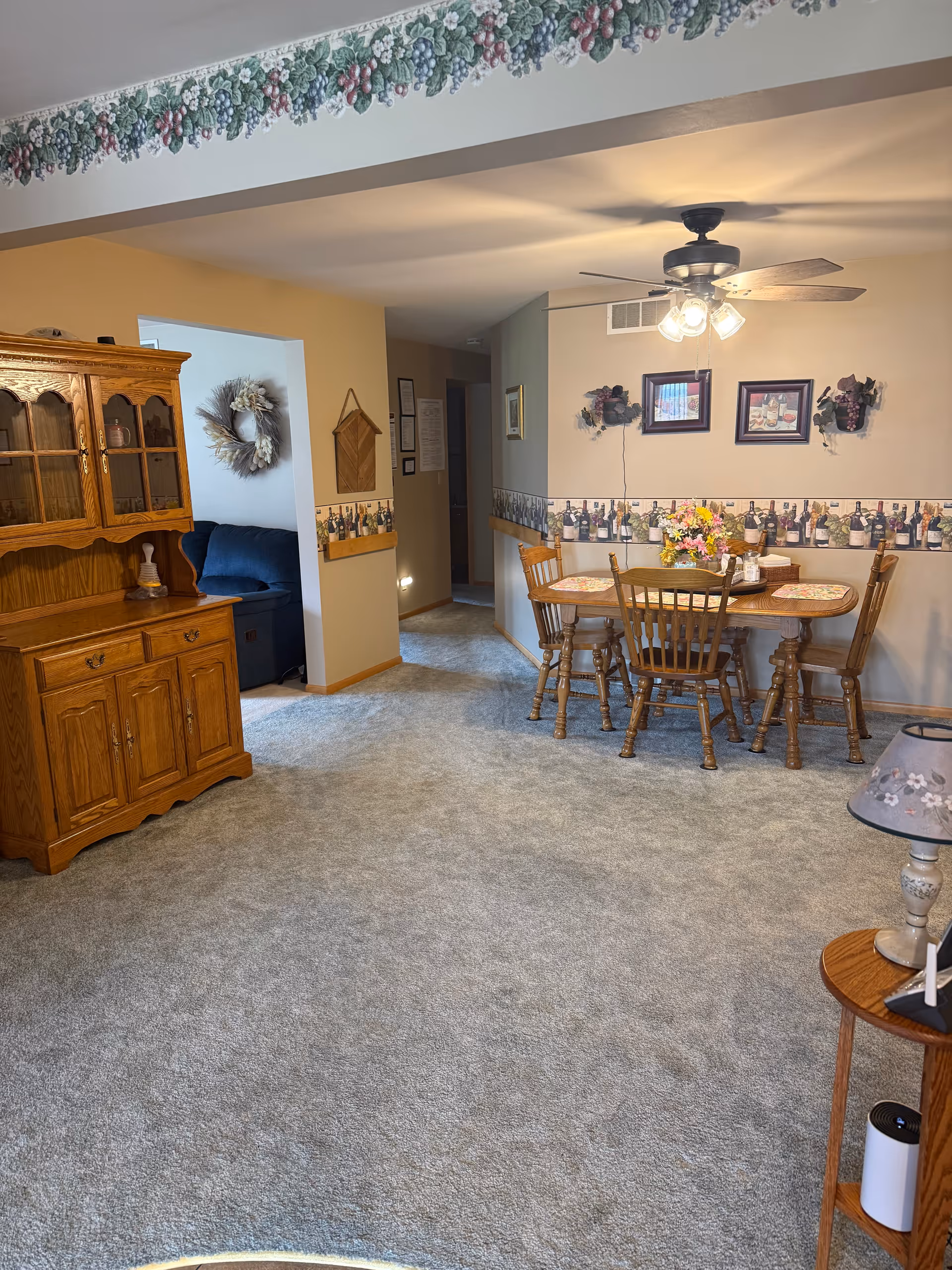 Dining area with wooden table and chairs, hutch, ceiling fan, floral centerpiece, carpeted floor