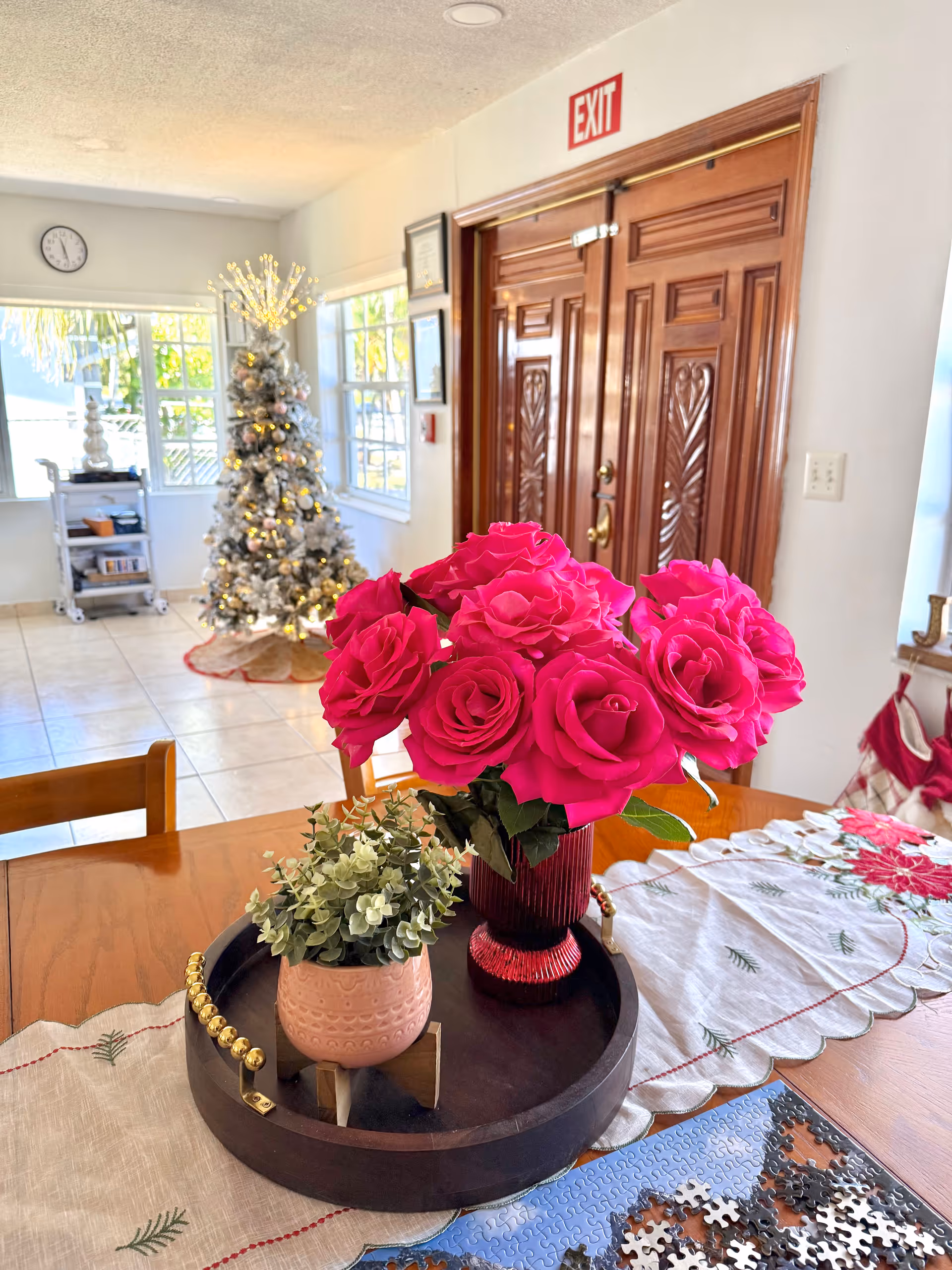 Interior of a senior living facility lobby with a Christmas tree, flowers, and wooden double doors.