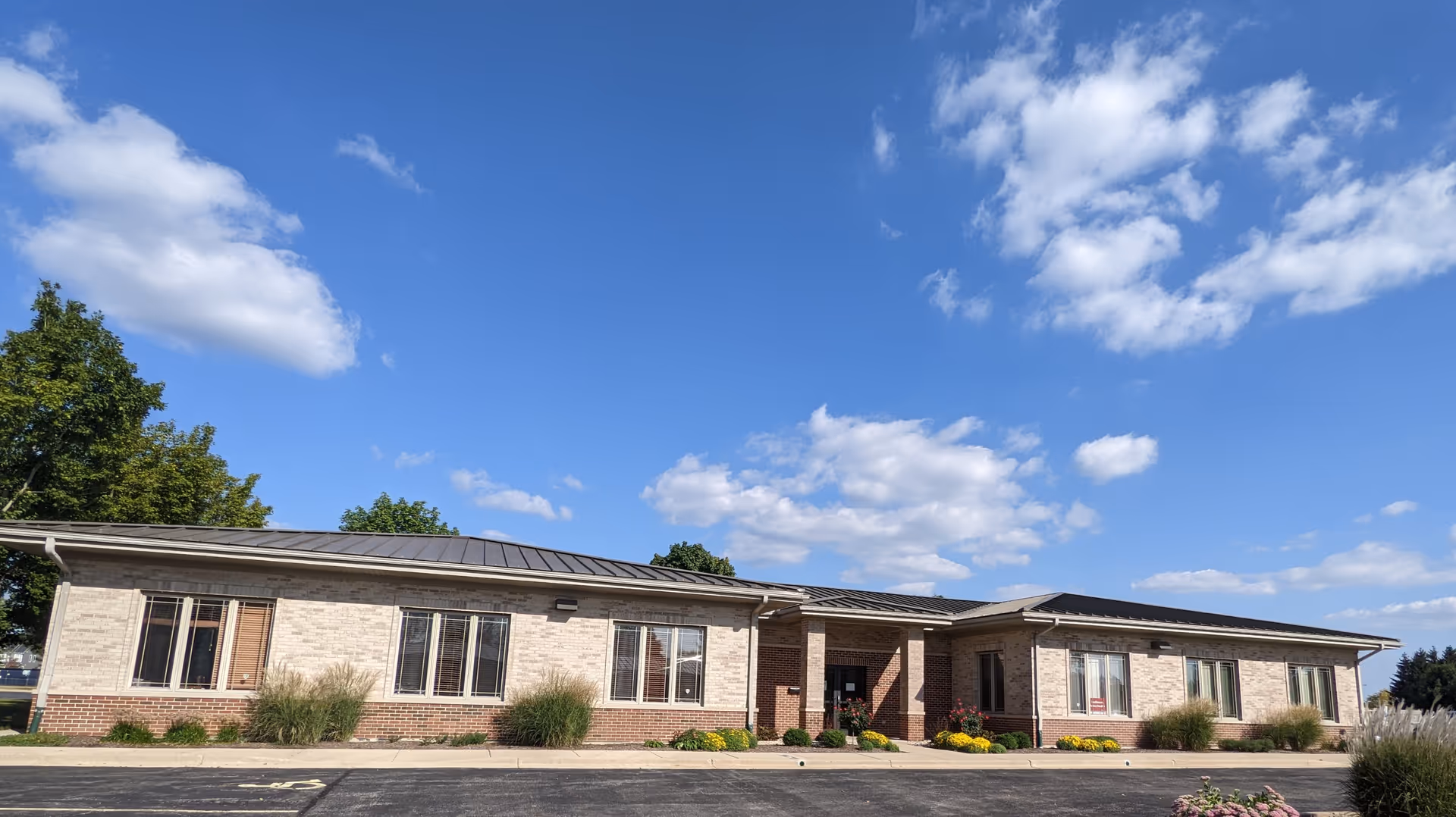 Single-story brick-and-stone senior living building with a front entrance and blue sky.
