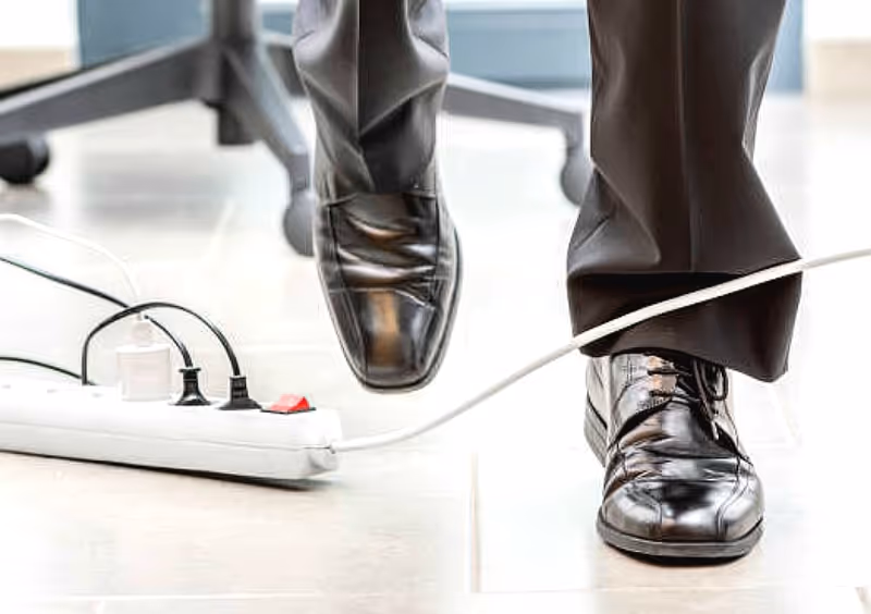 Close up of a person's dress shoes stepping over a power strip on a bright floor.