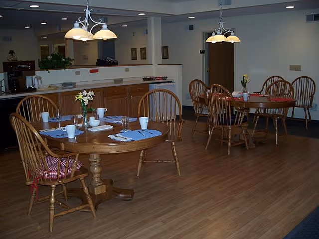 Assisted living dining room with round wooden tables set with placemats and flowers.