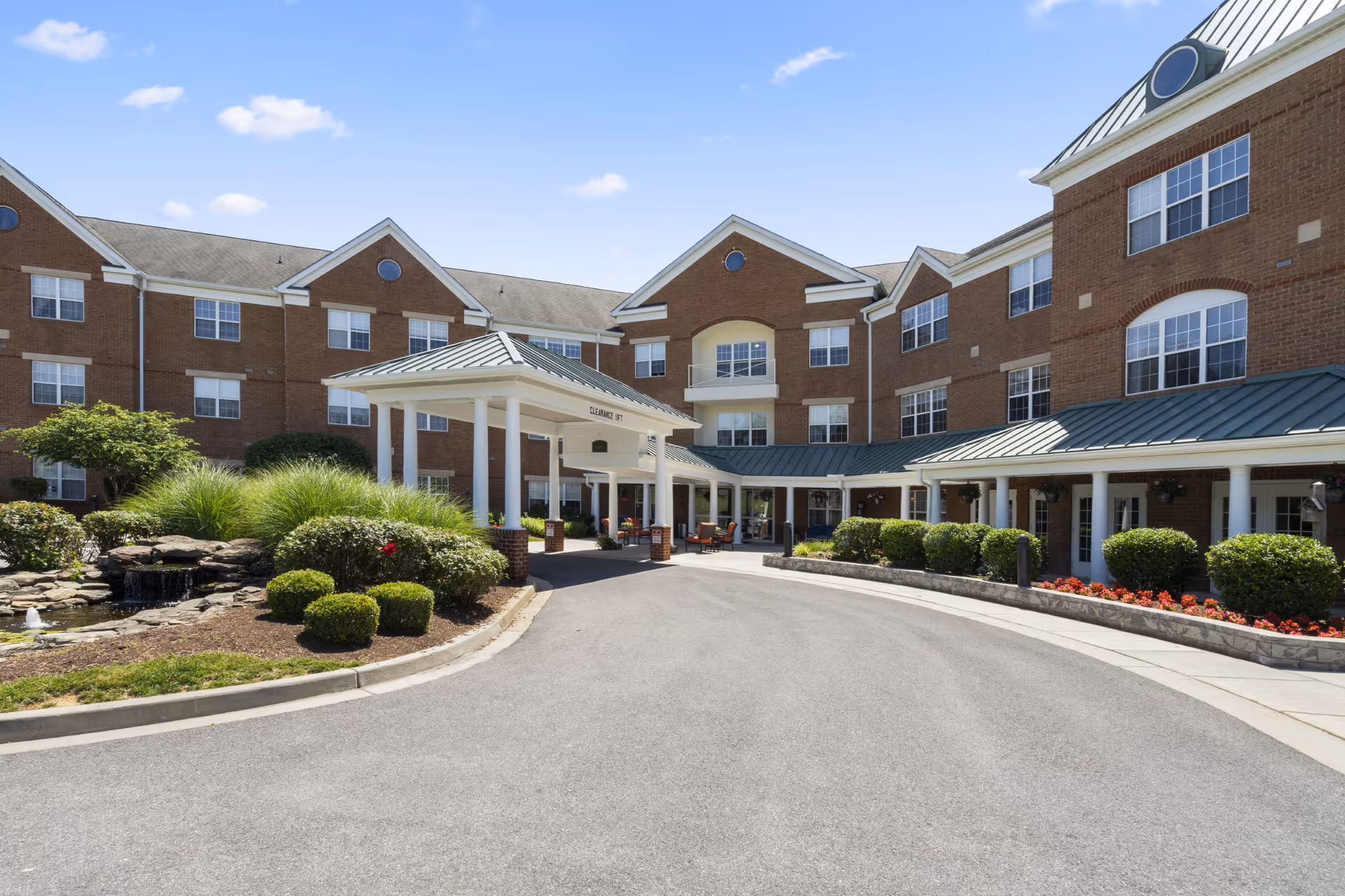 Exterior view of a brick senior living building with a covered entrance and landscaped driveway.