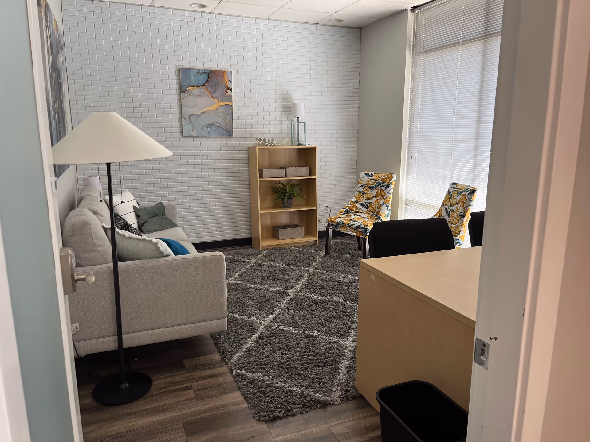 Cozy living room with gray sofa, lamp, bookshelf, rug, and two patterned chairs.