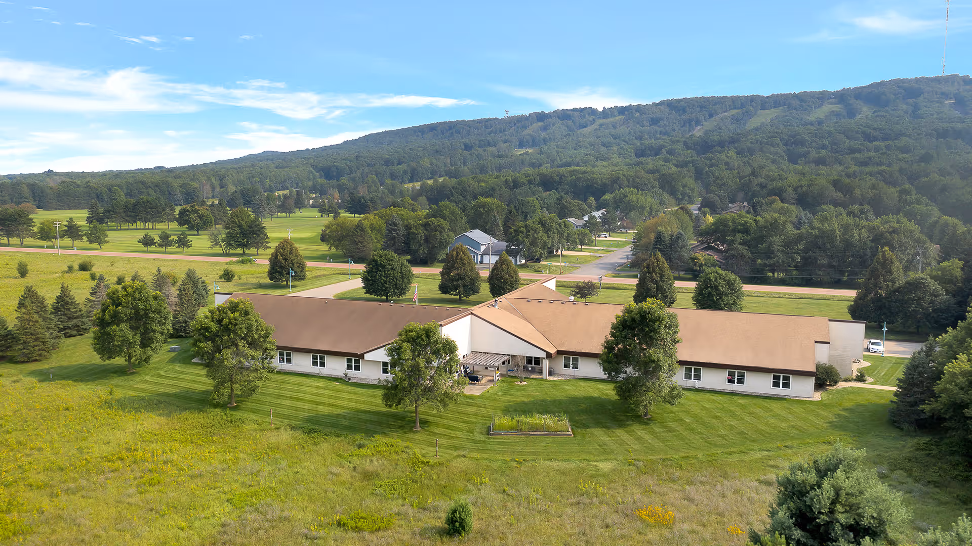 A single-story senior living facility sits in a manicured lawn with trees and hills.