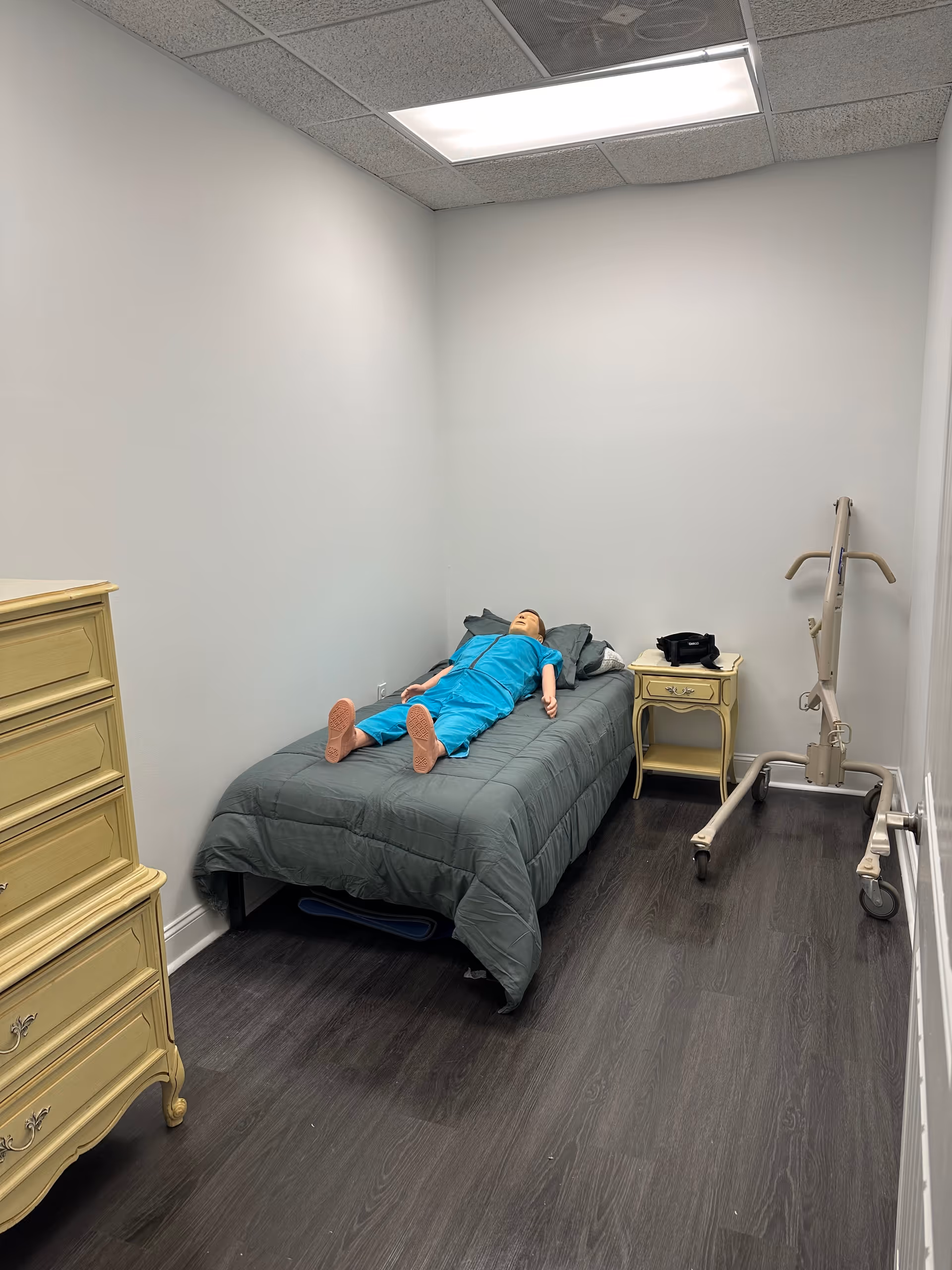 A sparsely furnished room with a bed, dresser, nightstand, and patient lift.