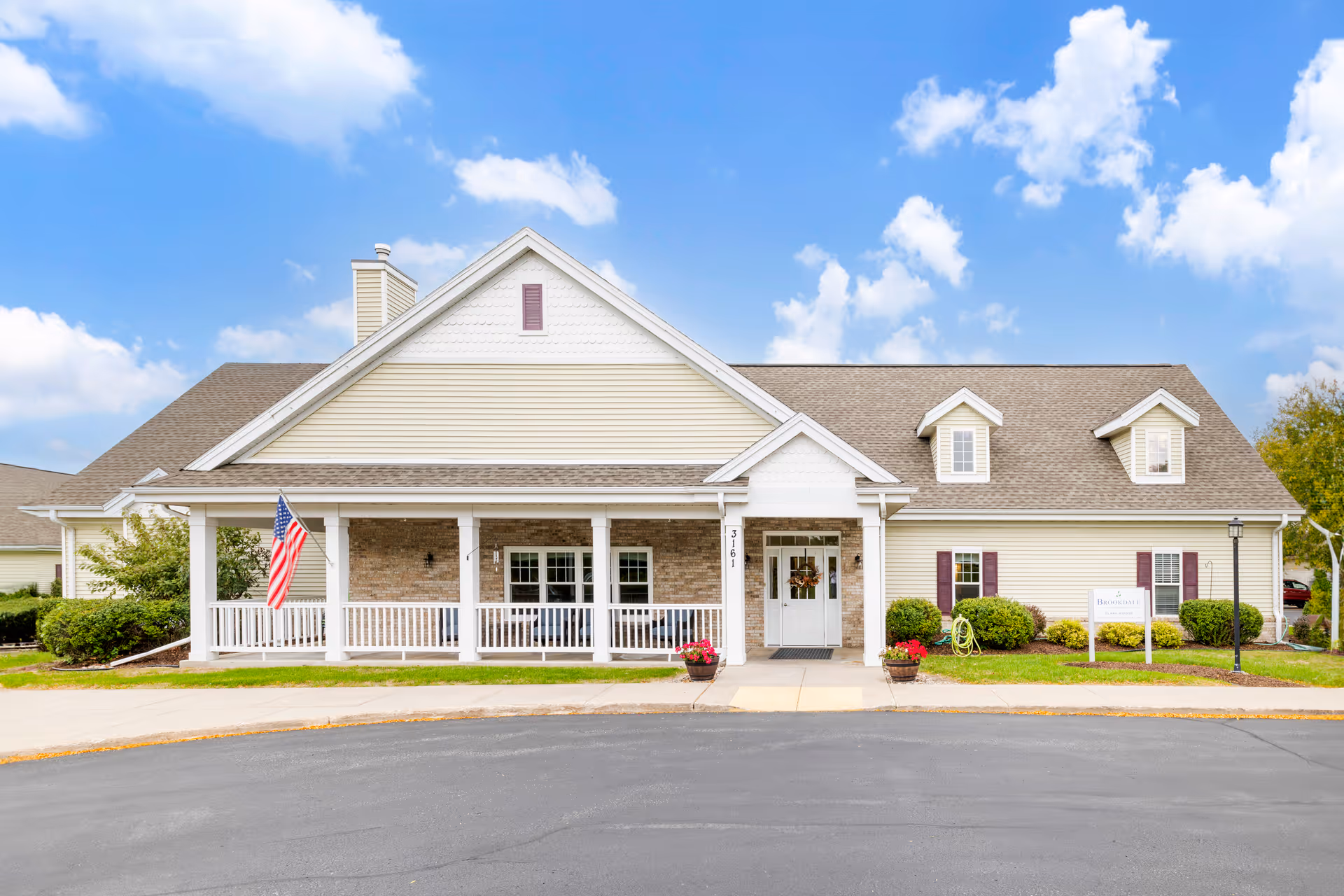 Front exterior of a single-story senior living residence with a covered porch and flag.