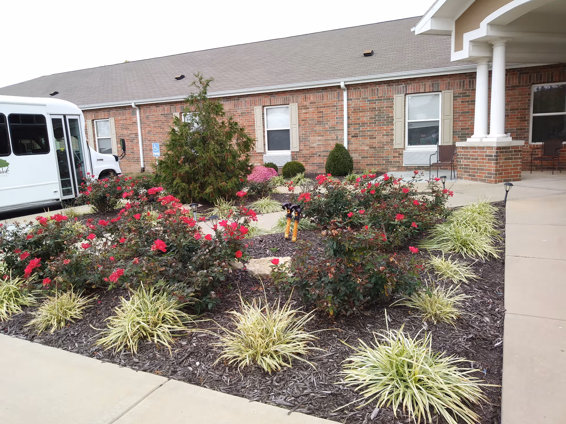 Brick senior living facility with a landscaped front garden and a parked bus on the left.