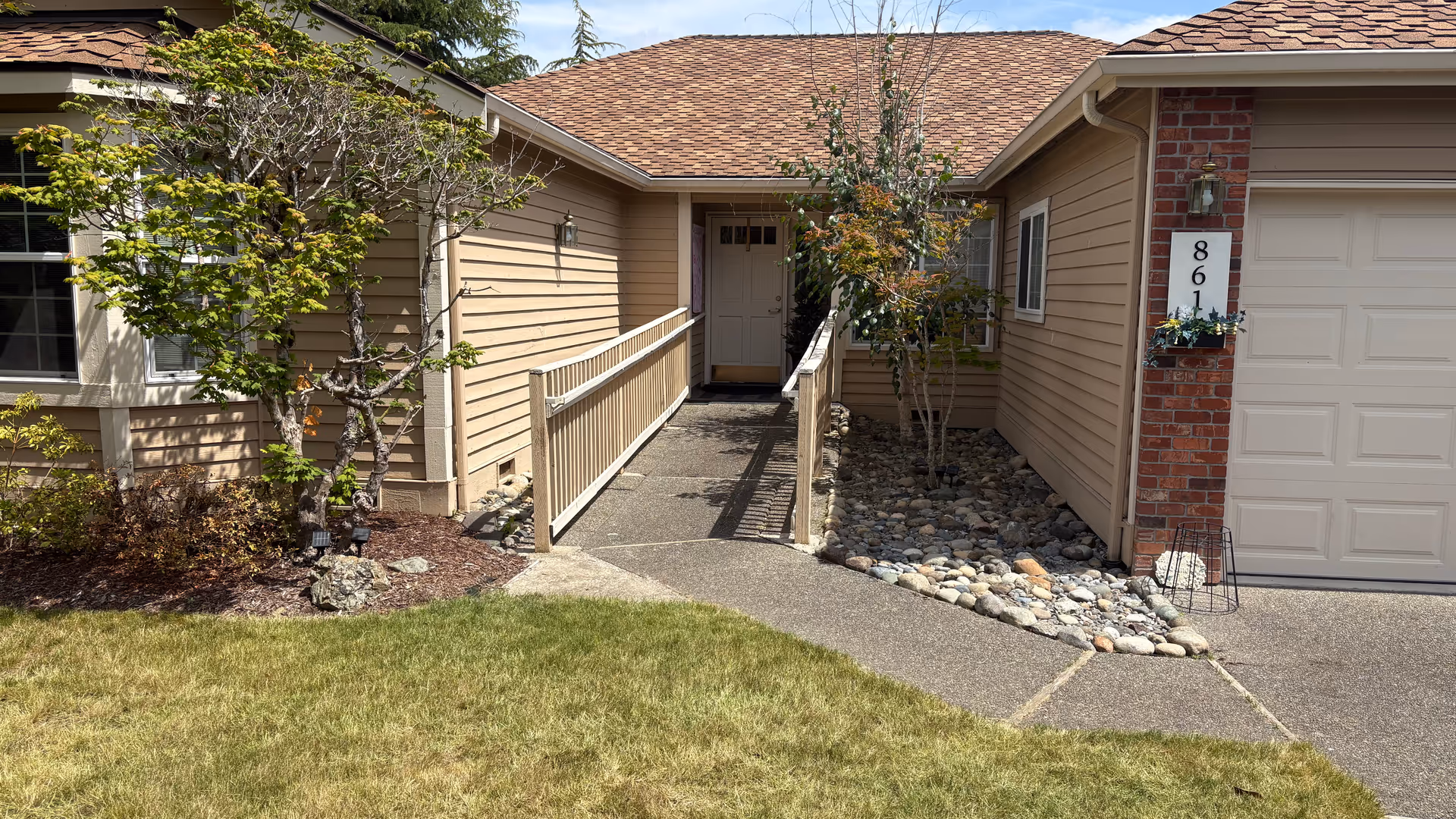 Front entrance of a beige senior living building with a ramp and landscaping.