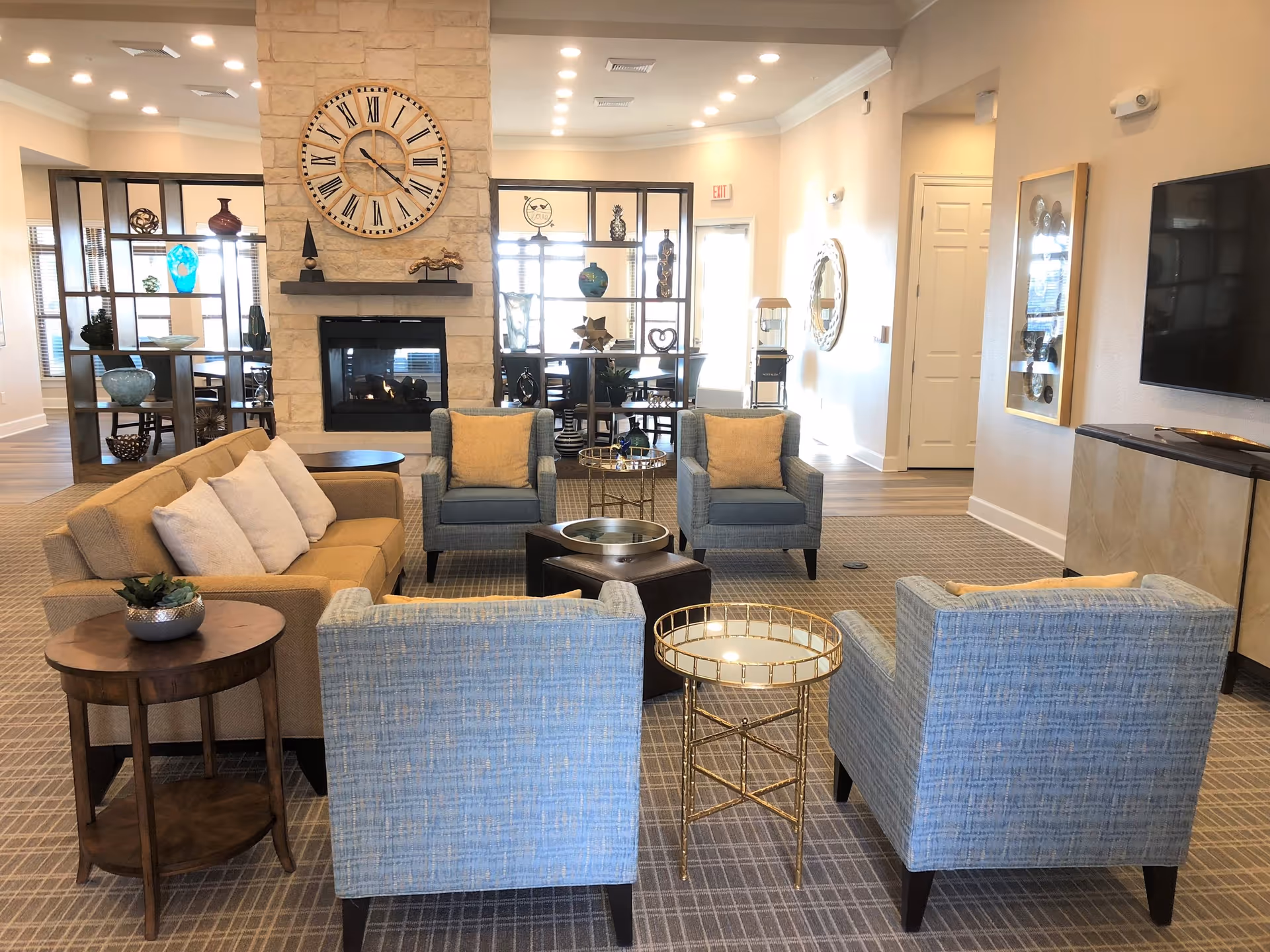 Senior living lounge with fireplace, large clock, and blue upholstered seating.