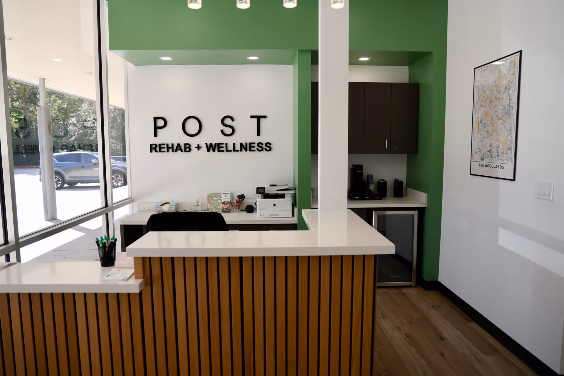 Reception desk in a bright lobby with POST Rehab + Wellness sign and green accents