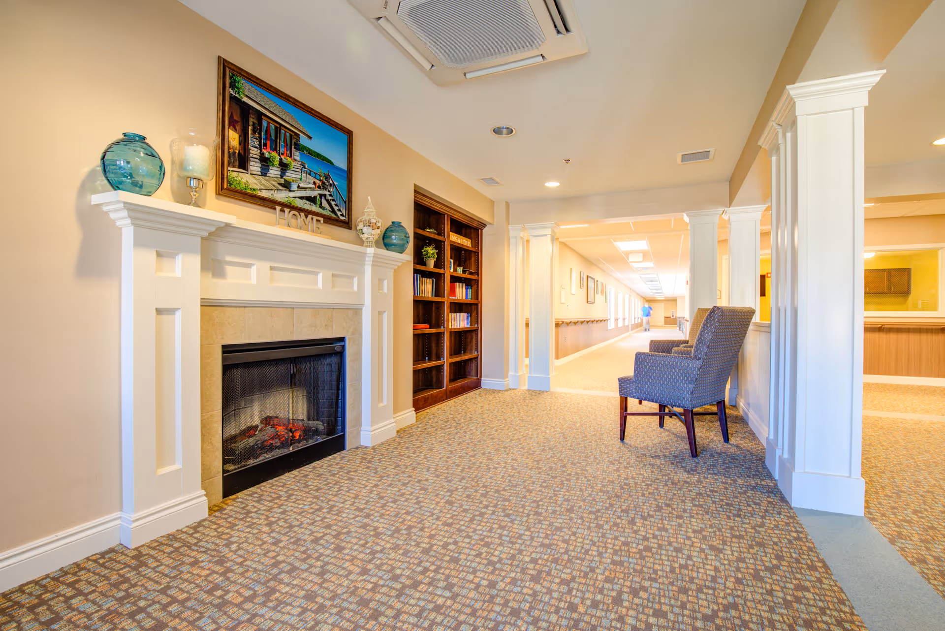 Cozy interior hallway with a fireplace, mantle decor, and blue upholstered chairs.