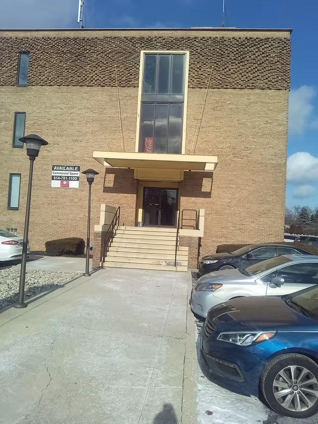 Brick senior living facility exterior with entrance stairs and parked cars.