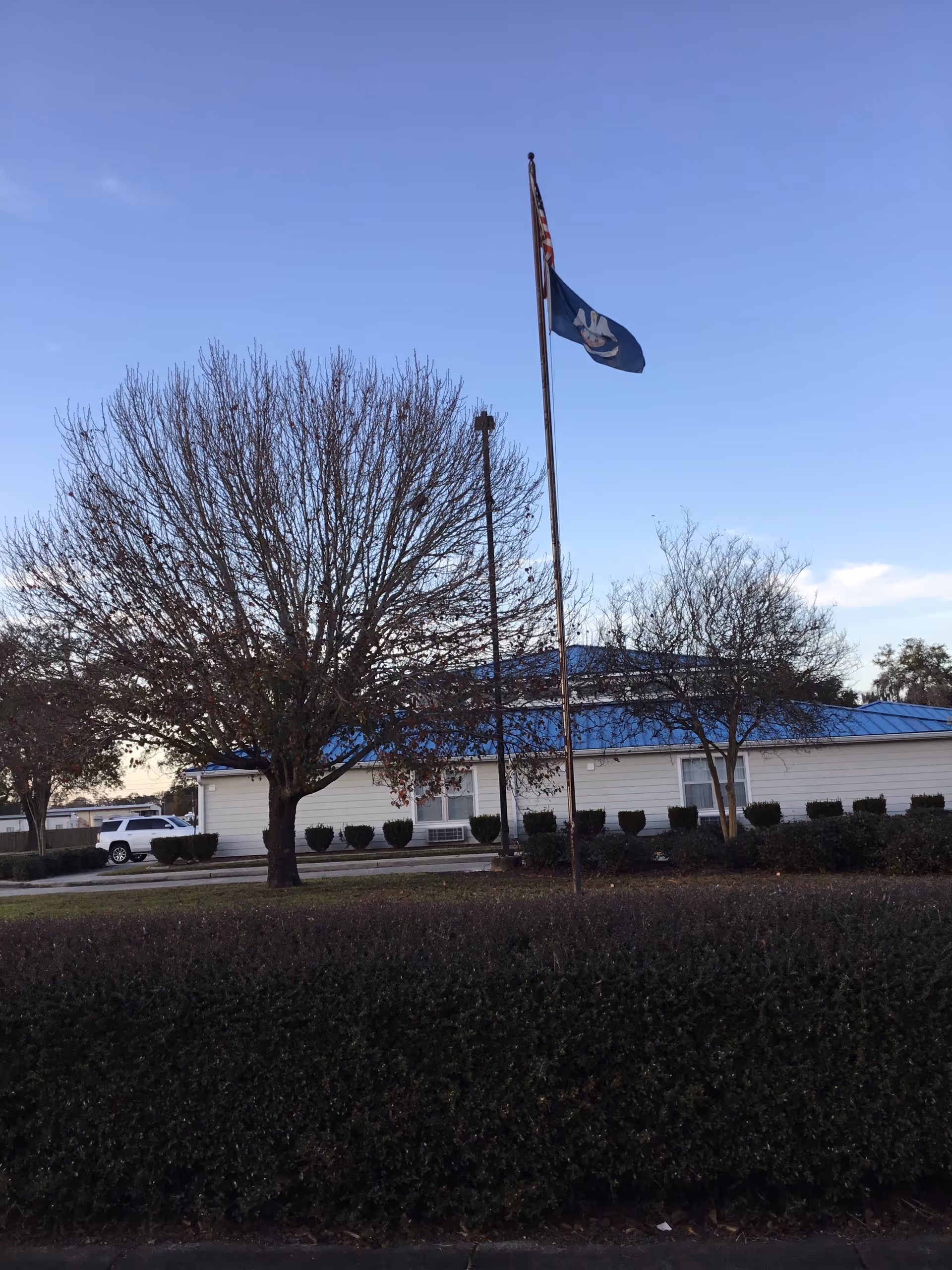 Exterior view of a single-story facility with a blue roof, flagpole, and trees.