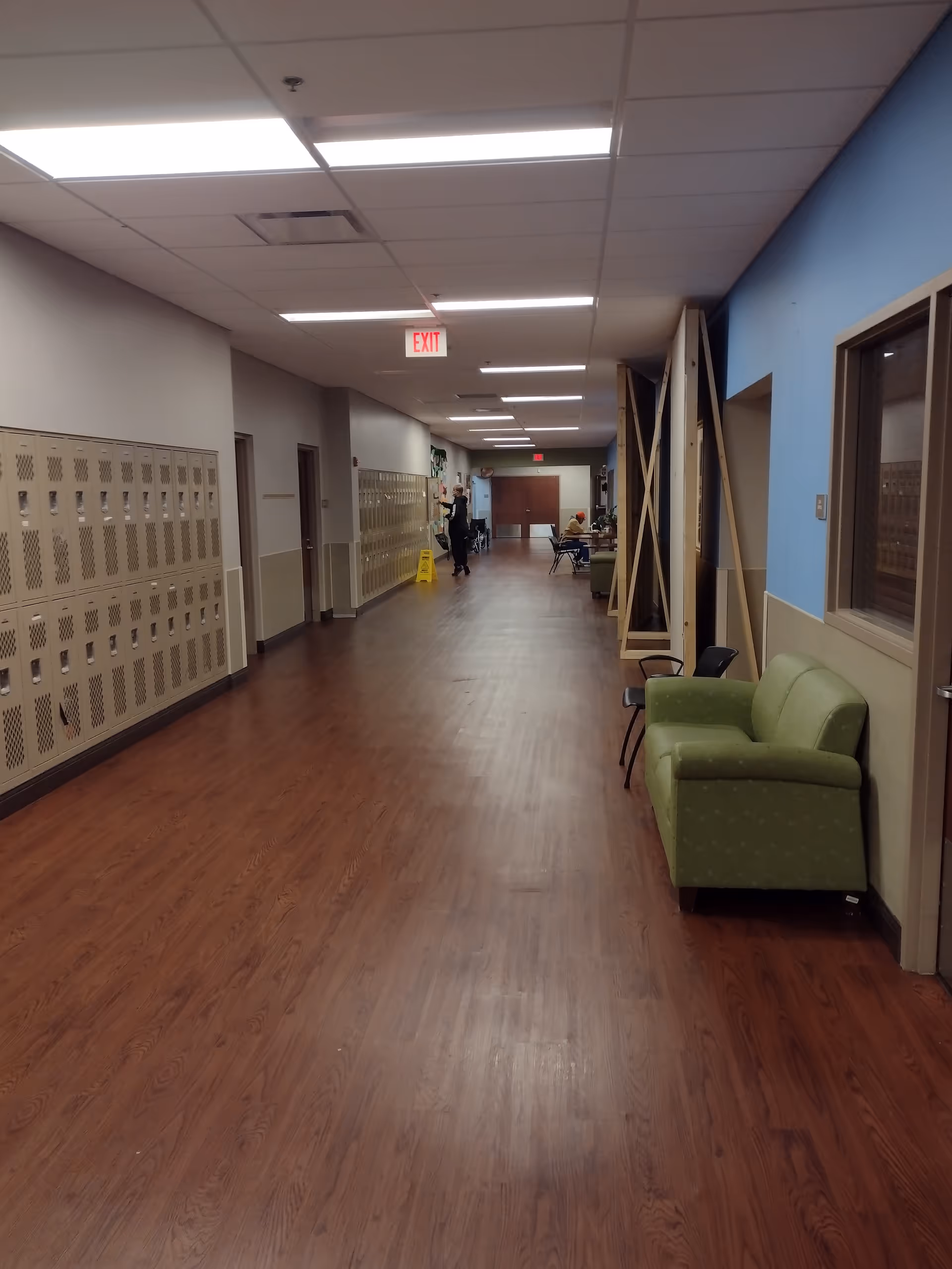 Long hallway inside Better Living Home Health facility with lockers, seating, and staff in the distance.