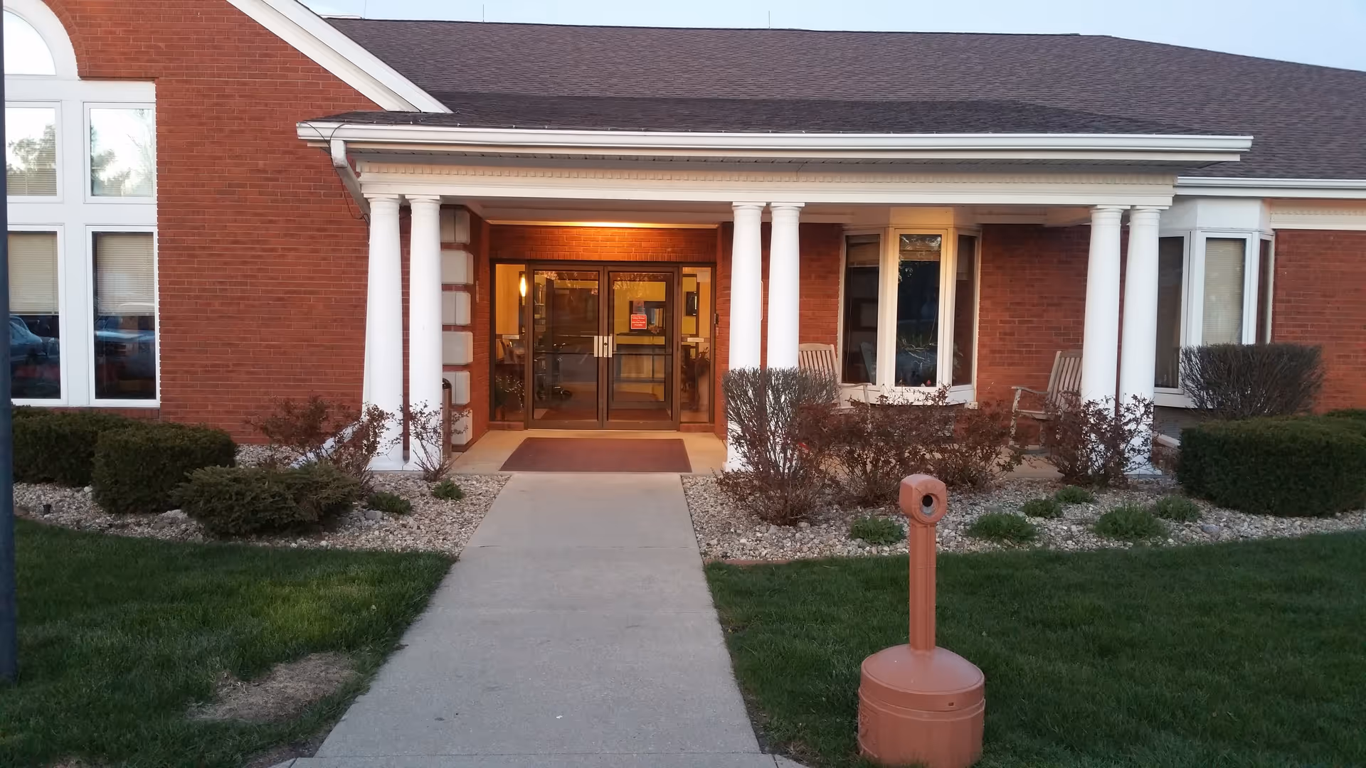 Brick senior living facility with white-columned entrance and landscaped walkway.