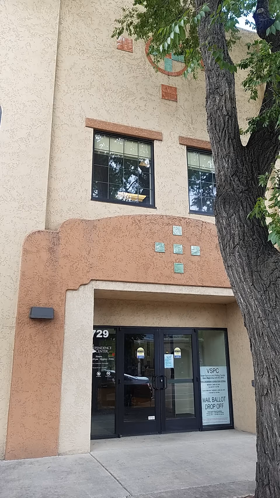 Exterior view of The Independence Center entrance with double glass doors and a large tree nearby.