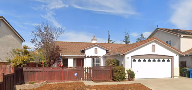 Front exterior of a single-story assisted living facility with a white garage and wooden fence.