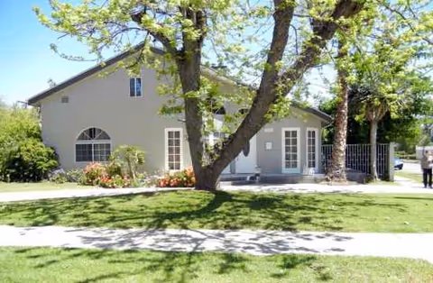 Be Well Senior Living exterior with large trees, walkway, and green lawn.