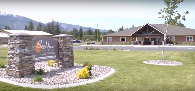 Exterior view of Maple Ridge Manor entrance with stone sign and manicured lawn.