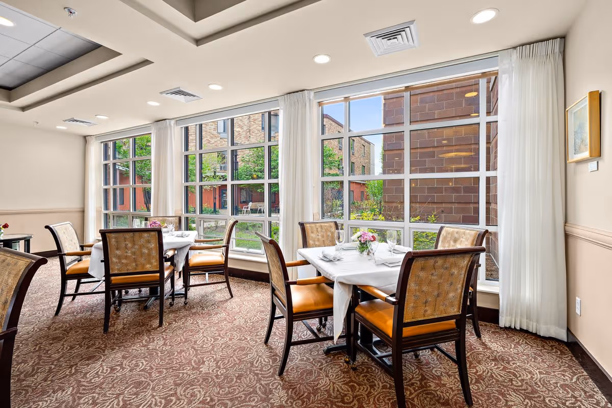 Small dining area with several set tables and chairs by large windows overlooking a courtyard.