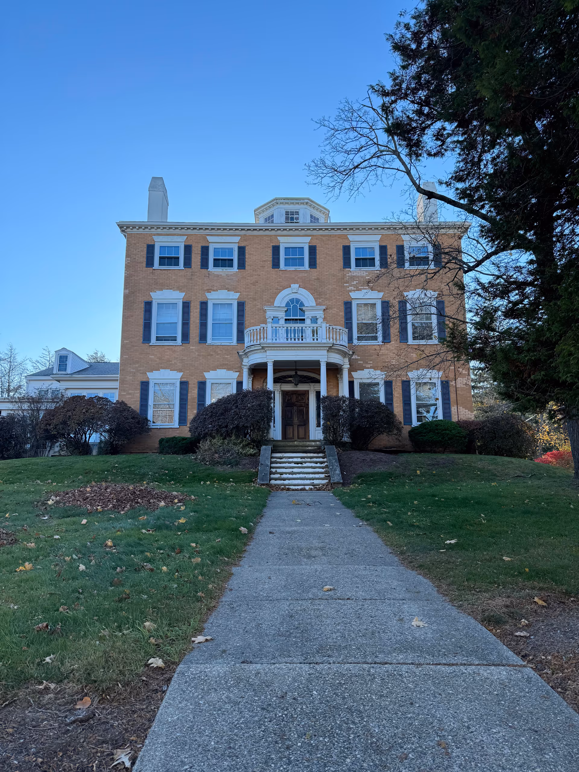 Brick three-story building with white trim and columned entrance, front walkway to stairs.