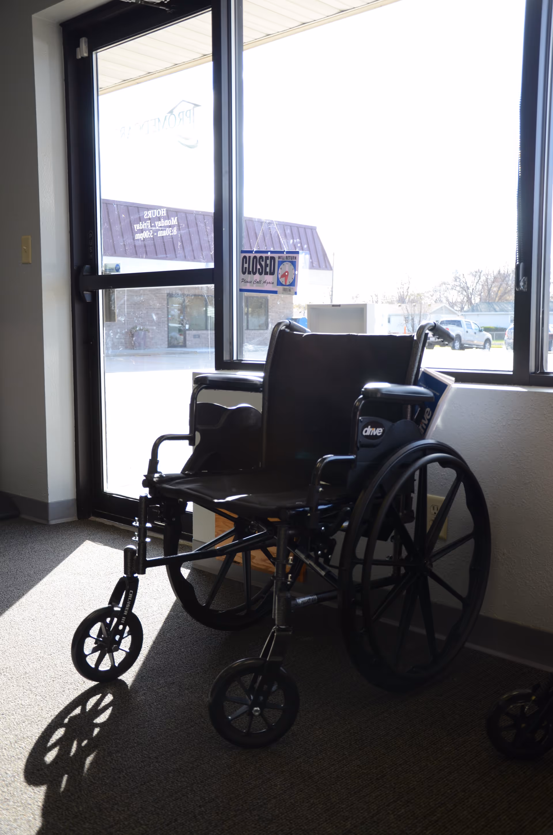 Wheelchair parked near a glass door inside a facility lobby, sunlight outside.