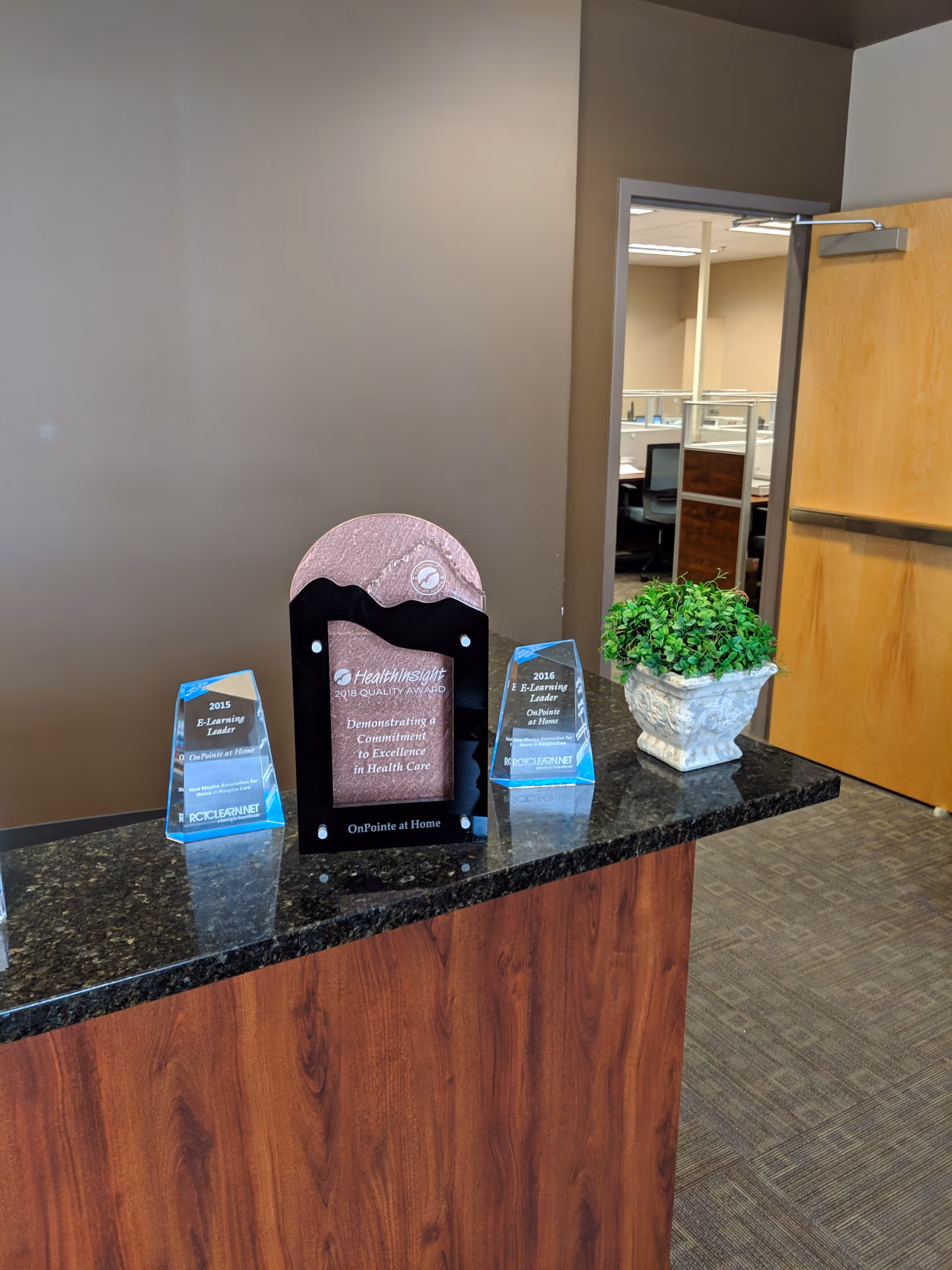 Reception counter with glass awards and a potted plant in a facility lobby.