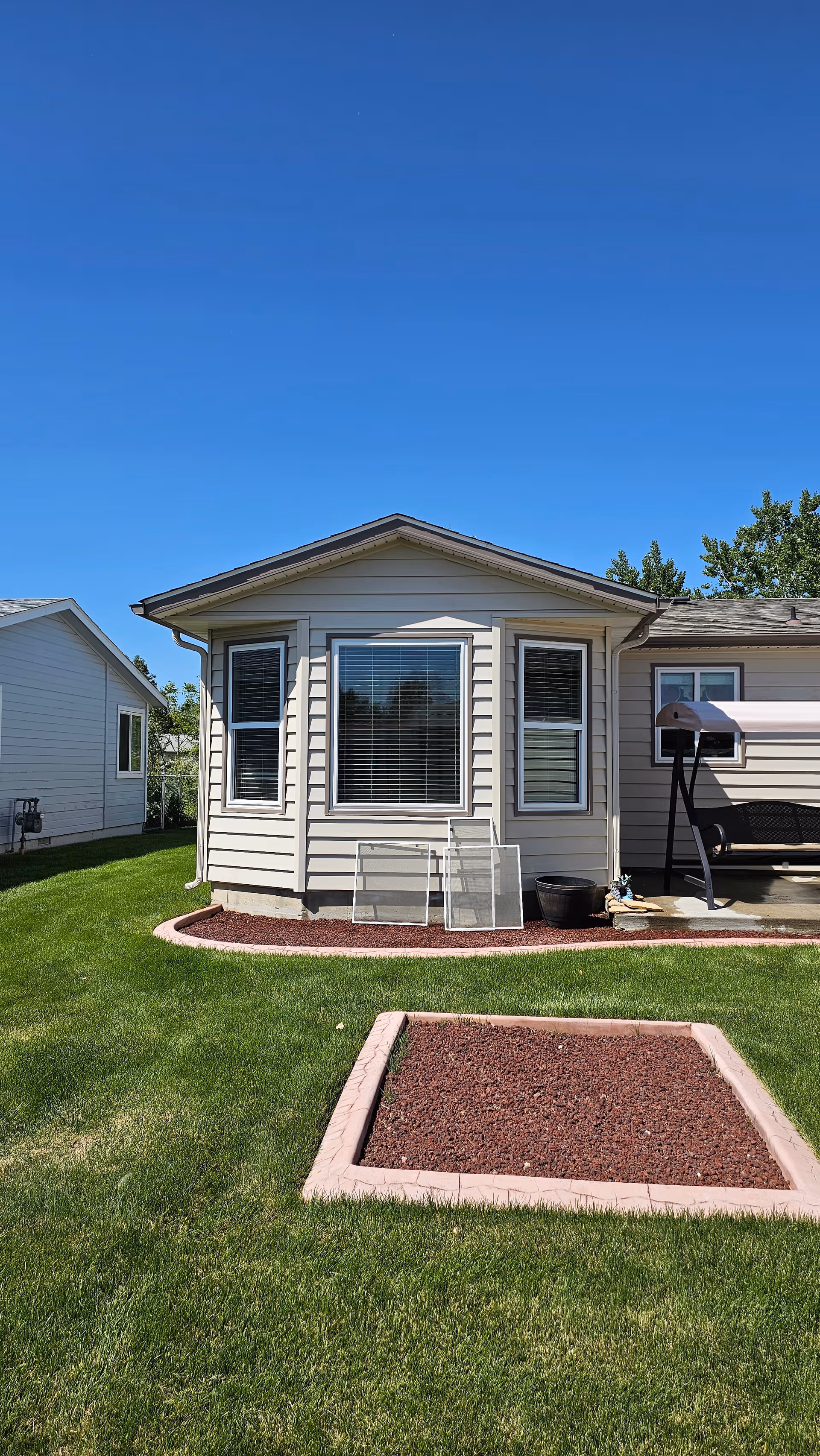 Exterior view of a small beige house with windows, lawn, and a front yard garden.