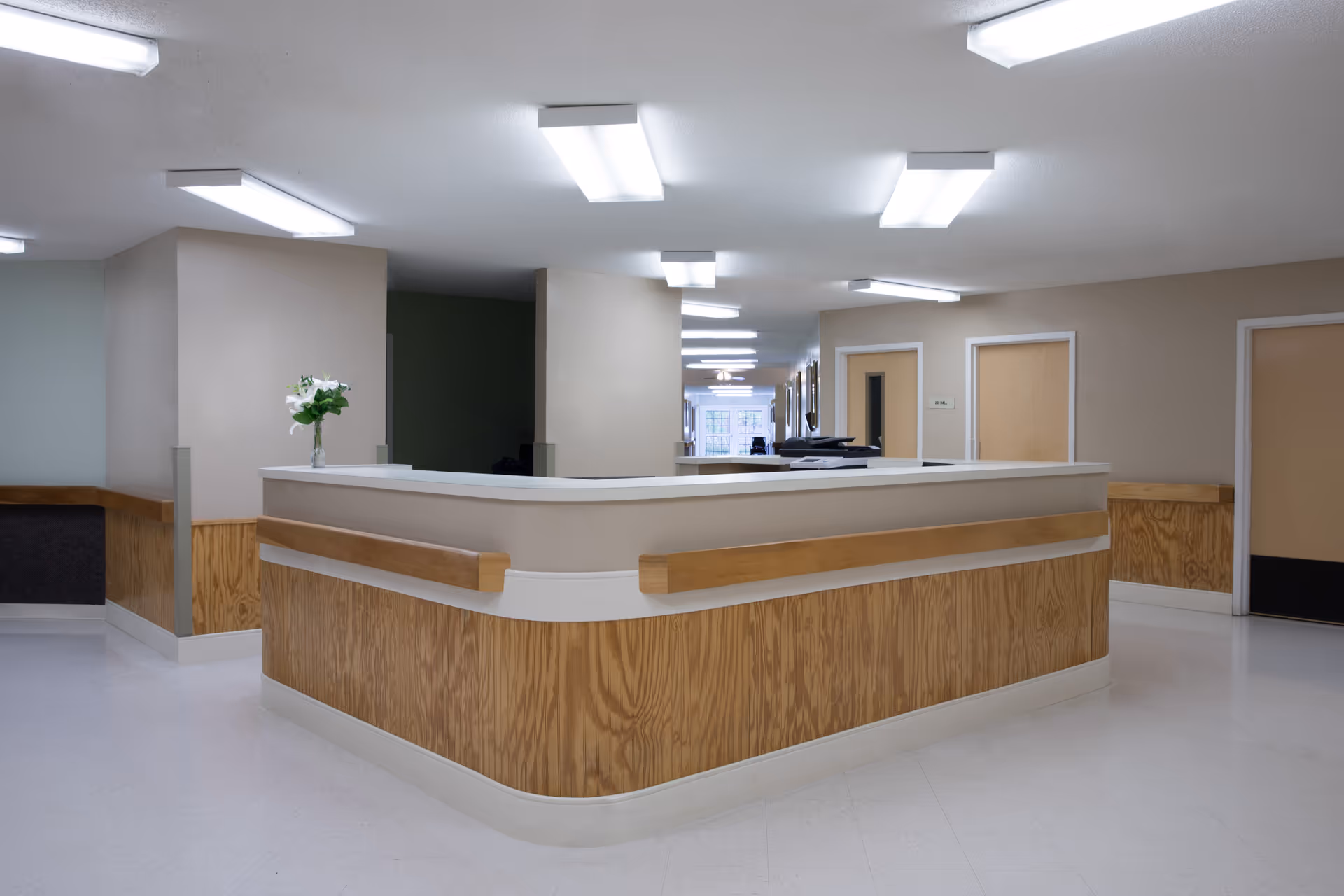Curved wooden reception desk in a well-lit hallway of a senior living facility.