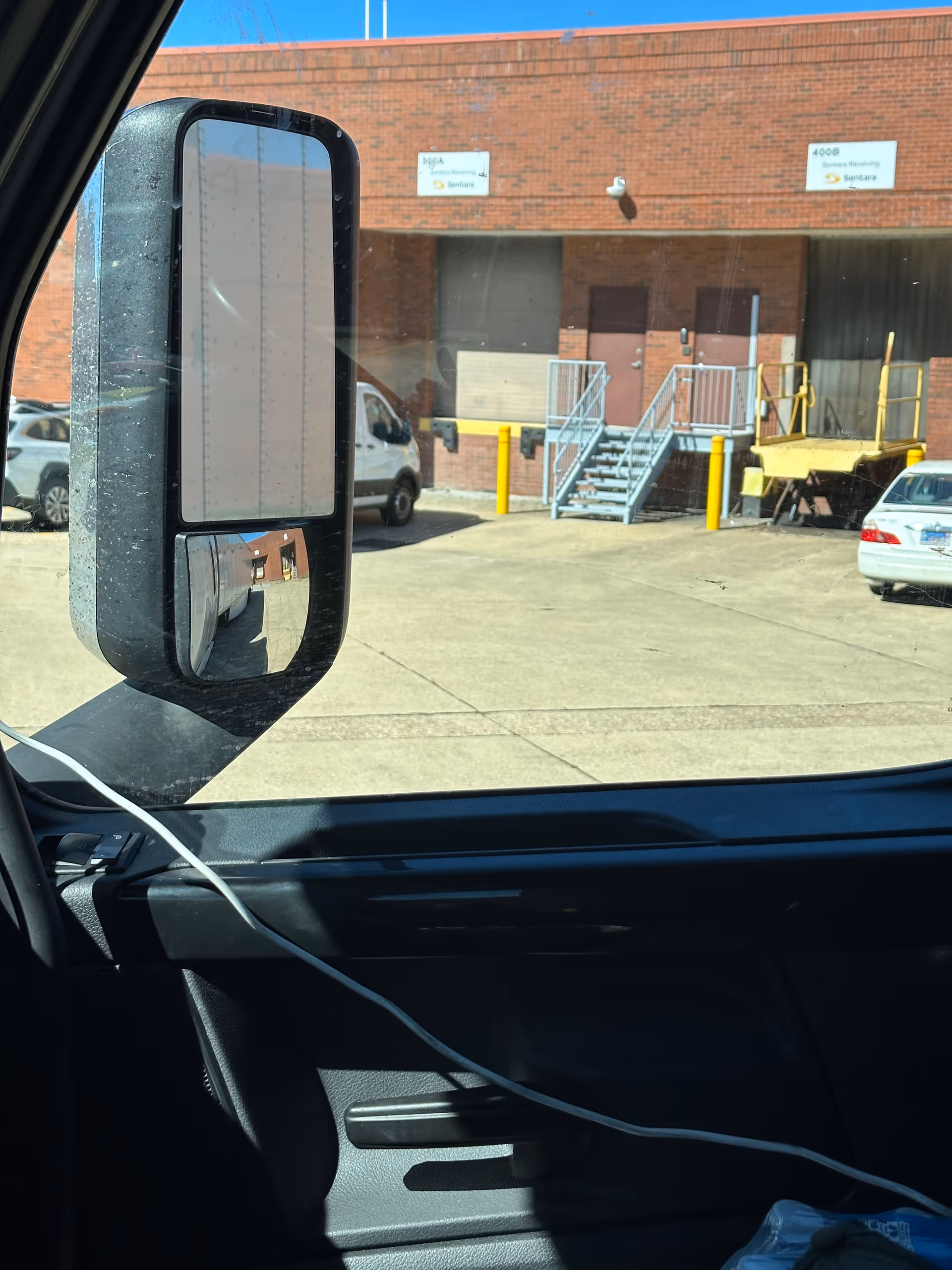 Driver's side view from inside a vehicle showing a brick loading dock and parked trucks