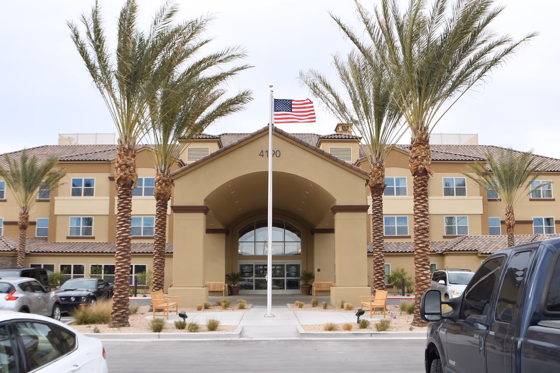 Facade of Vista Park Retirement Community with arches, palm trees, and an American flag at entrance