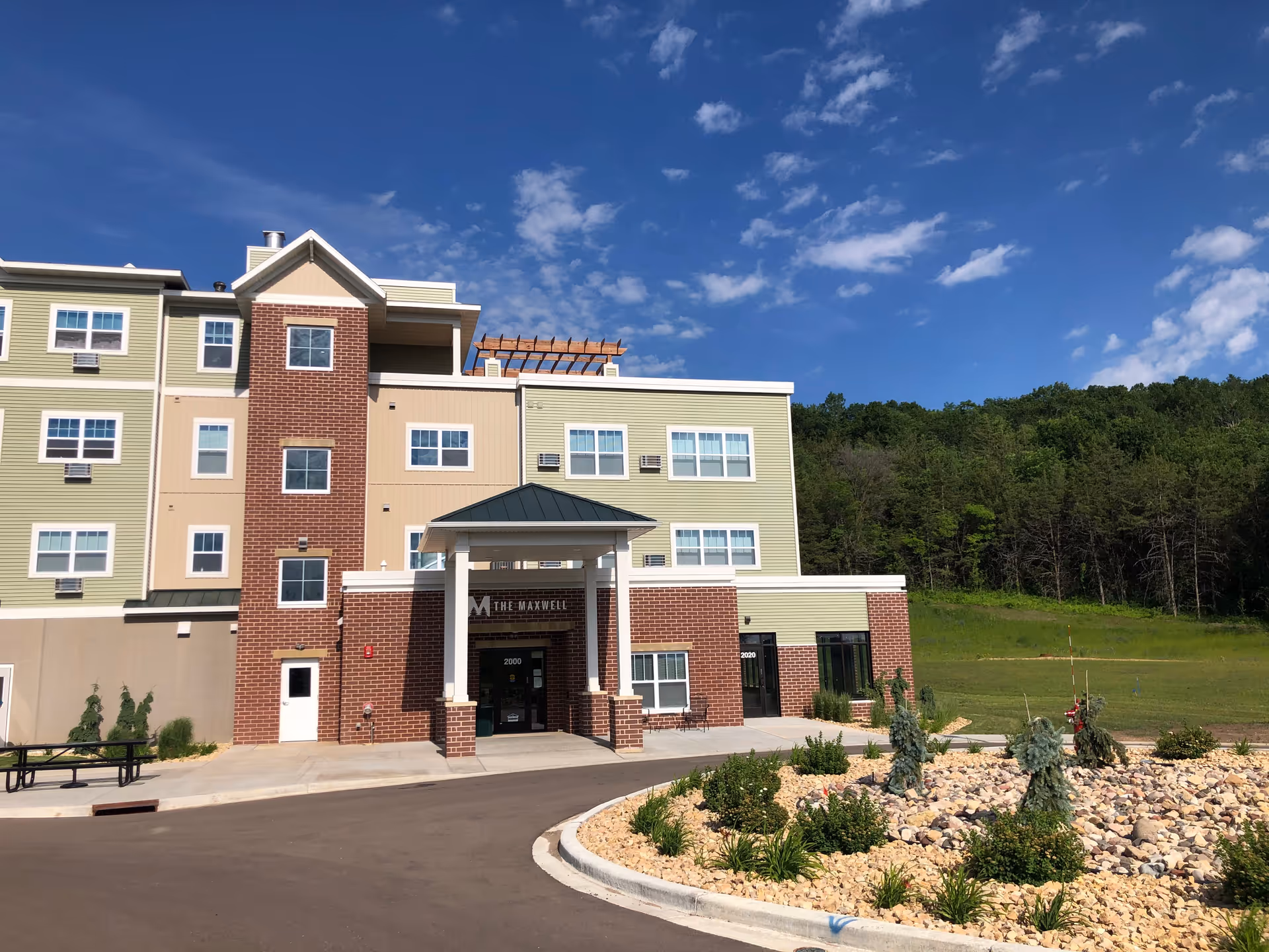 A multi-story senior living building with brick entry, green siding, and landscaped front.